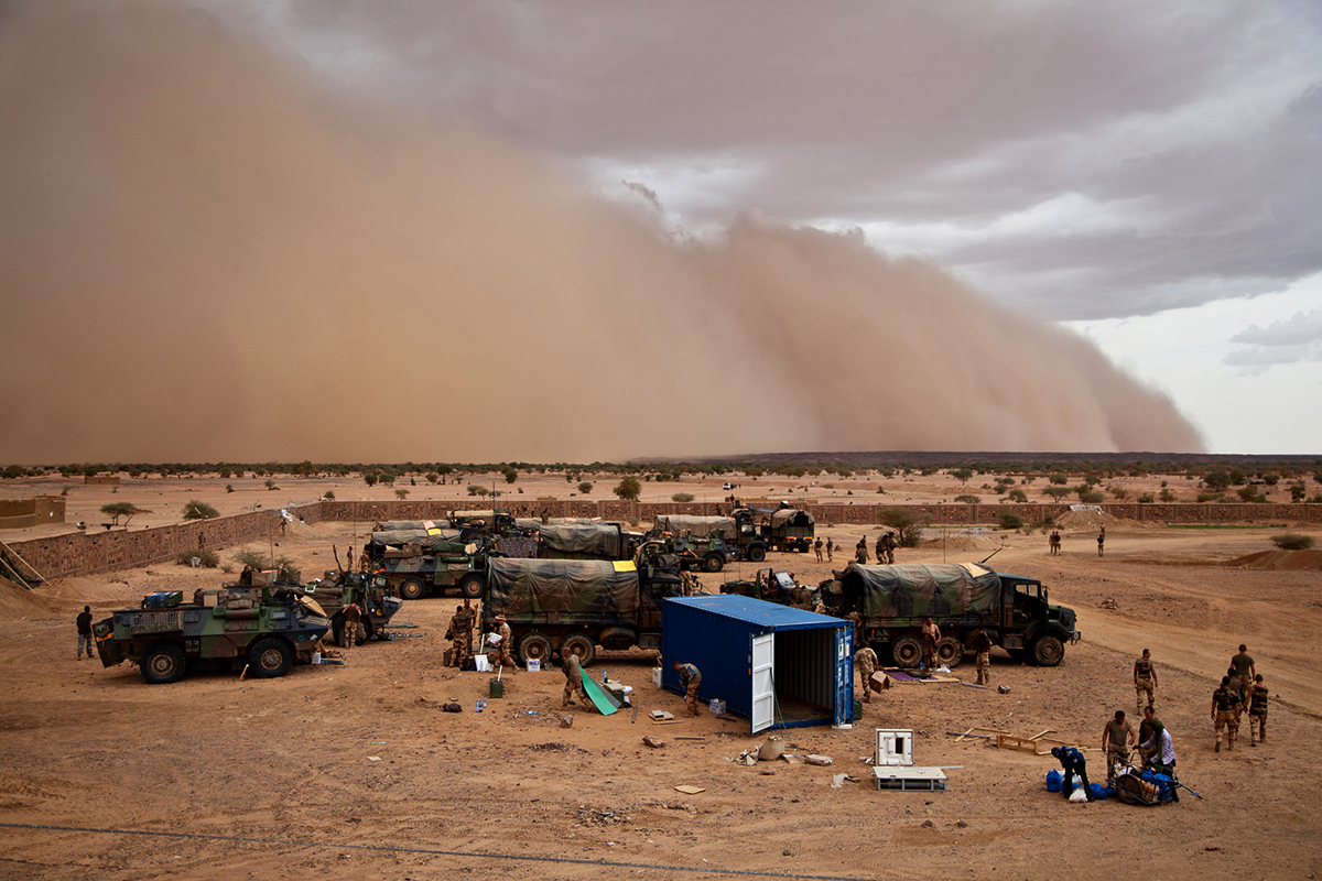 Military personnel pack up a camp as a large sandstorm cloud approaches in Kidal, Mali