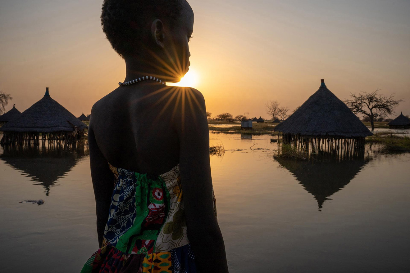 A girl looks at a flooded village in the sunset