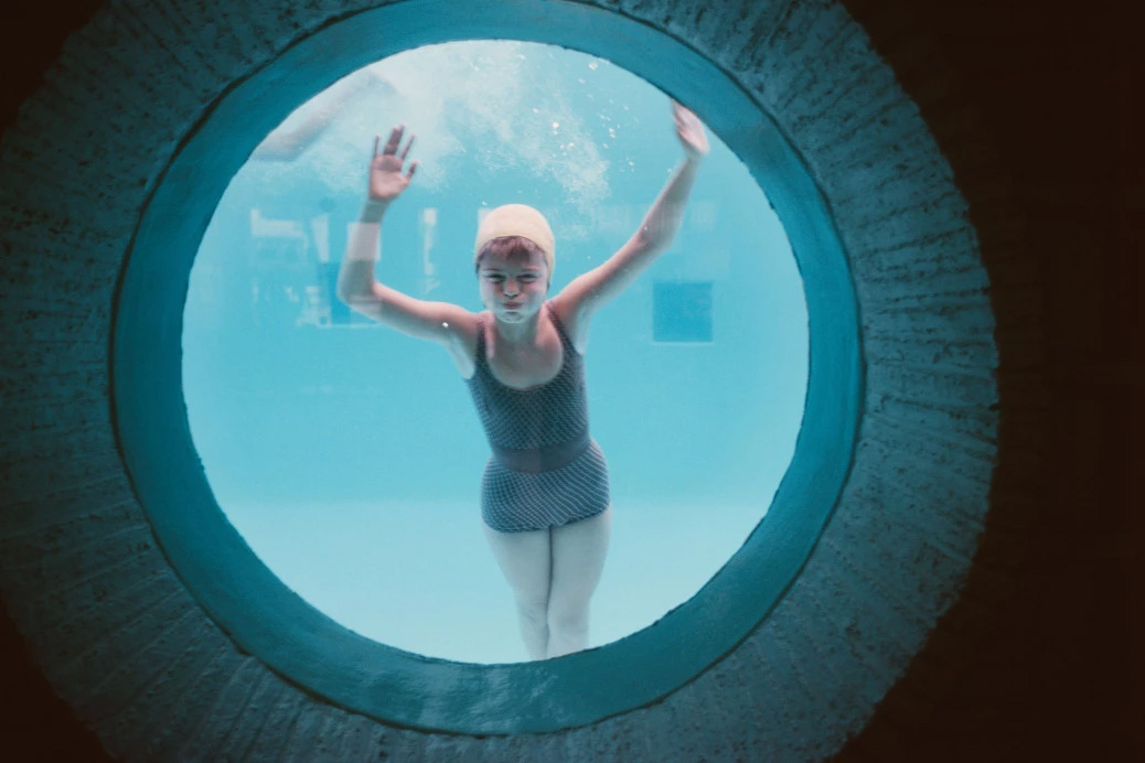 A lady in a swimming pool looking through a glass