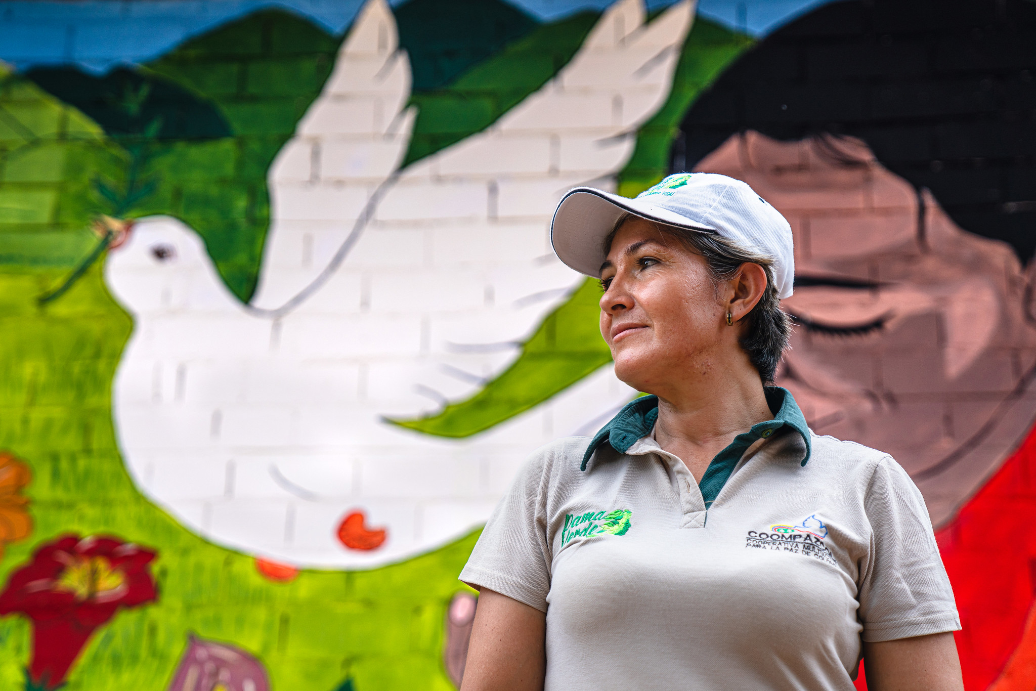 A woman with a white cap, standing in front of the mural with a dove