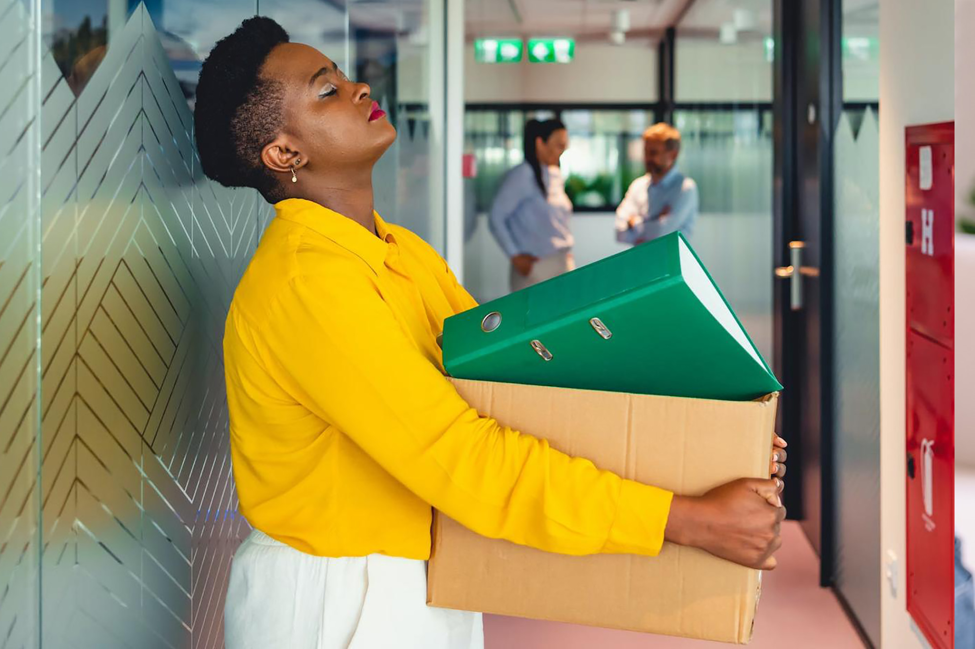 A woman is seen carrying a box that is full of binders in an office space.