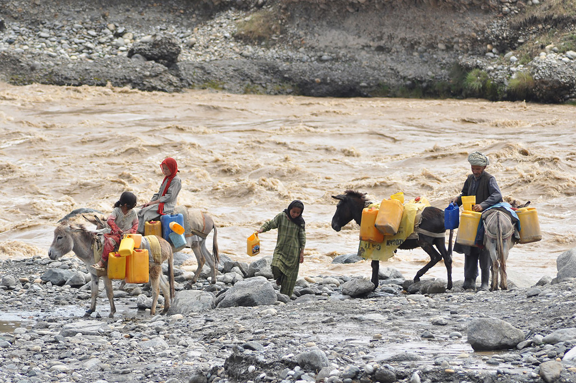 Young girls and a man collect water in jugs transported by donkeys 