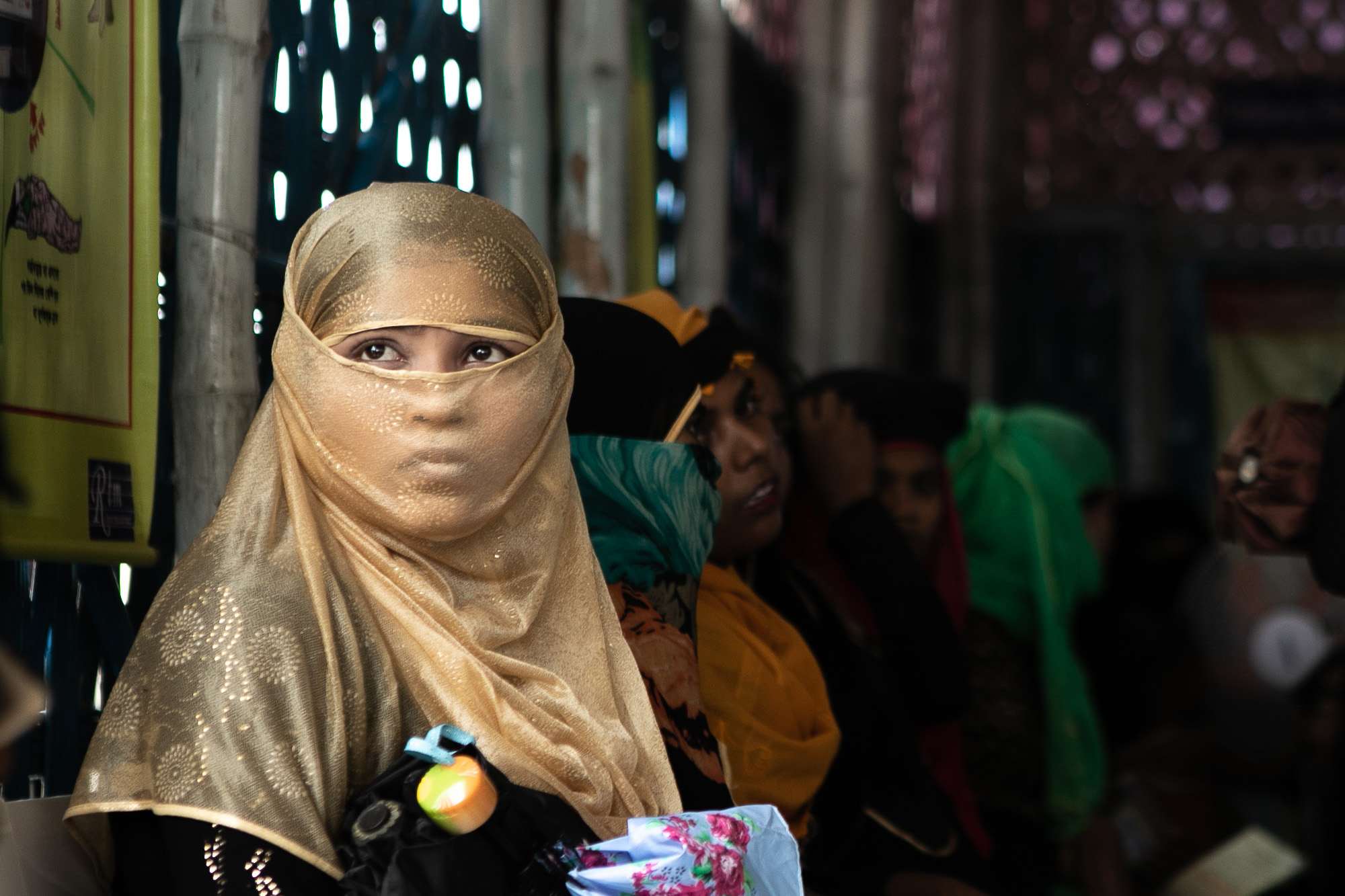 A young girl sitting with a group of people at a refugee camp in Cox's Bazar.