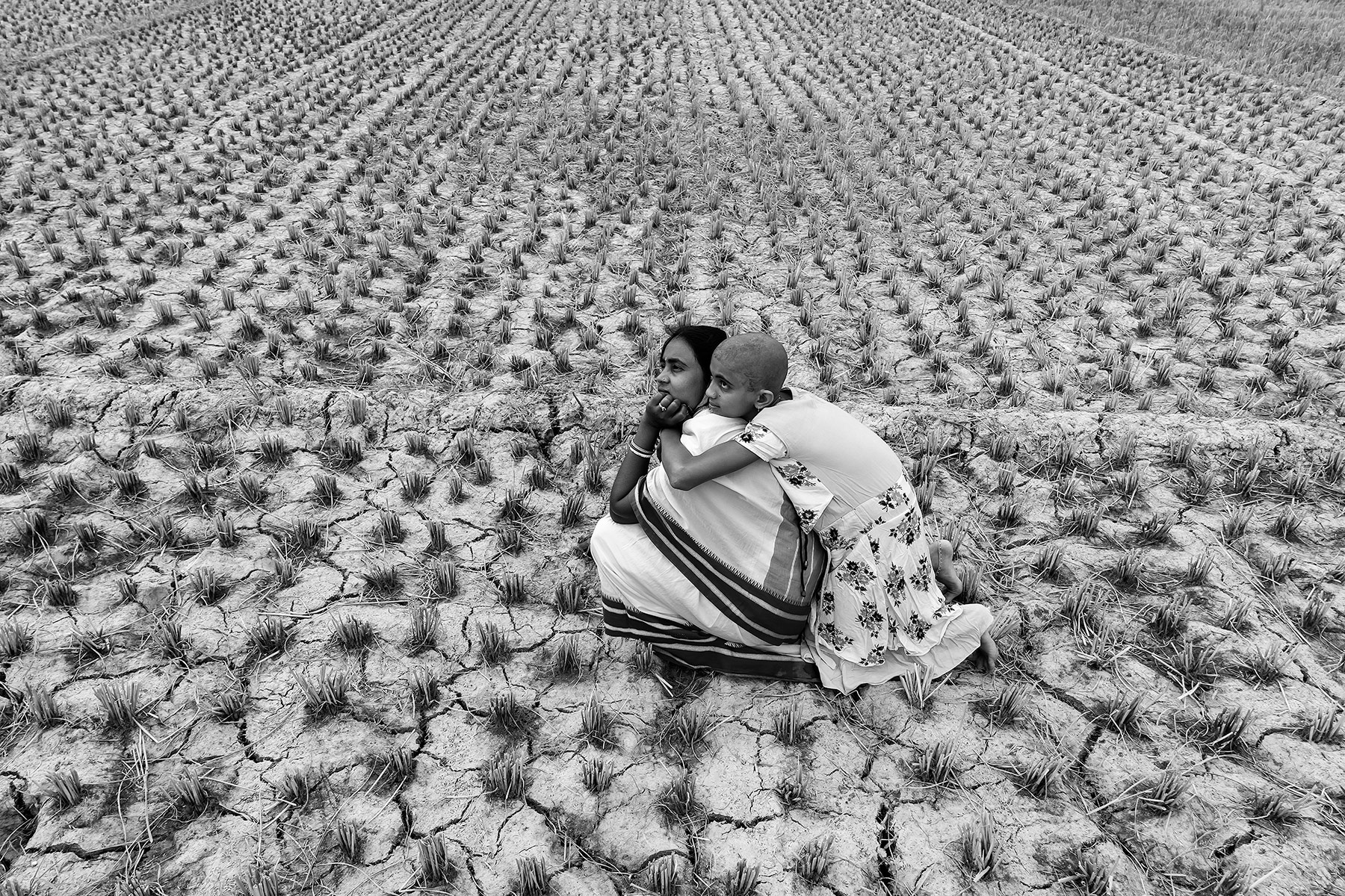 A woman and her daughter sitting on dried and cracked land