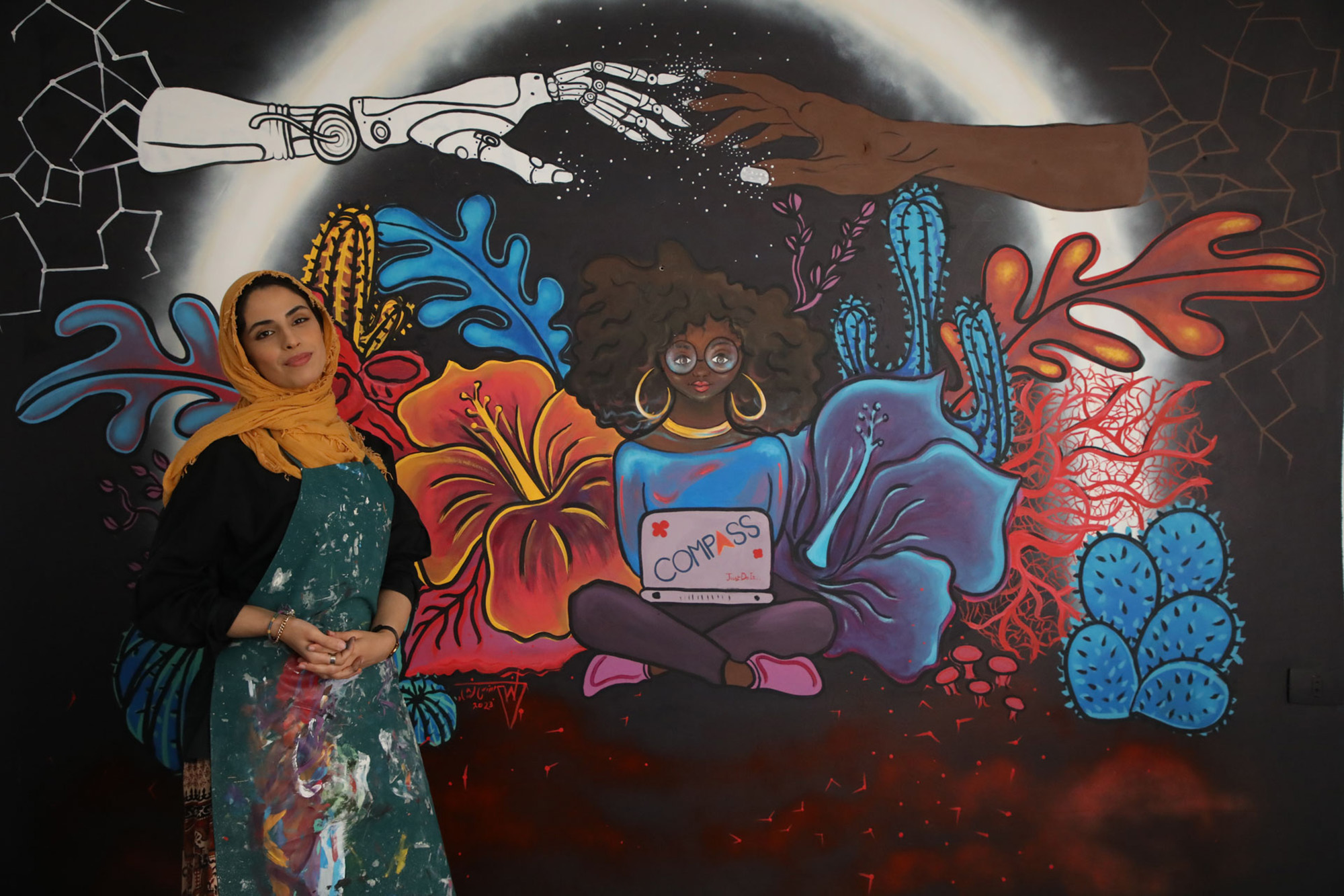 A woman standing before her mural. The artwork portrays the strength and connection of women worldwide .