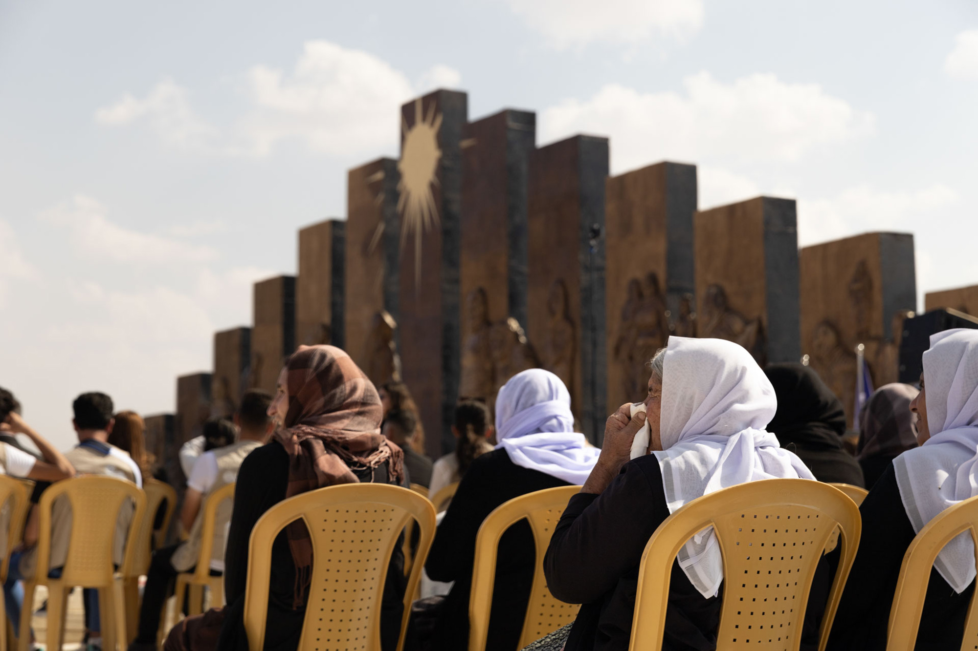 A group of women sit in front of a memorial monument that pays homage to the resilience of the Yazidi community during the Daesh occupation of Iraq.