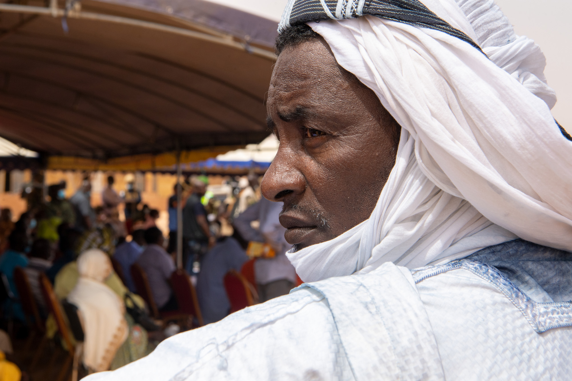 Alt: Close-up of a refugee in a Nigerian camp with a crowded tent in the background.