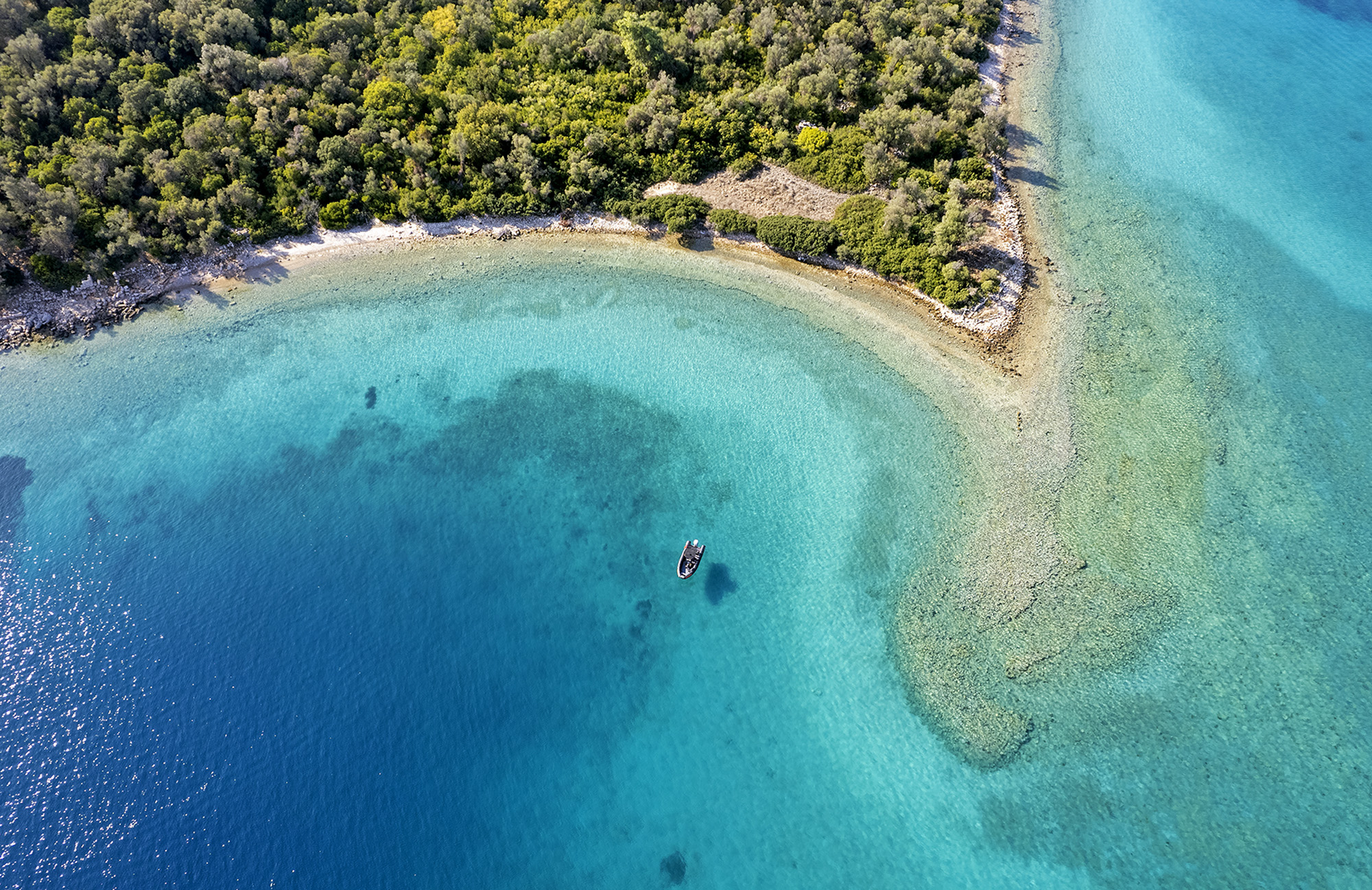 Aerial view of a green Turkish island with a boat in the water.