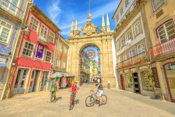 Deux enfants en vélo et une femme se promenant dans une ville colorée