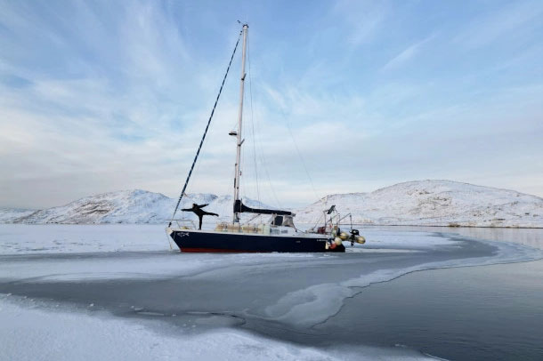 Une personne pose à l'avant de son voilier dans un environnement glacial