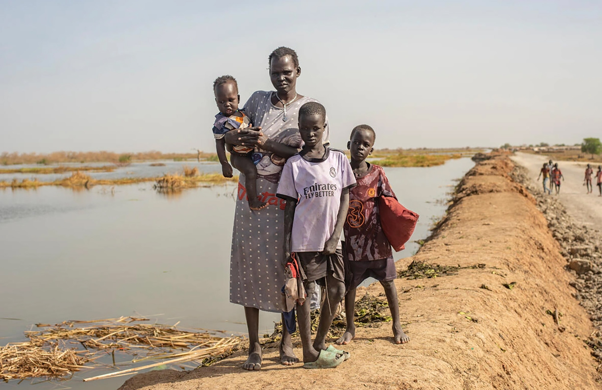 A South Sudanese woman and her three children in front of a body of water next to a narrow path.