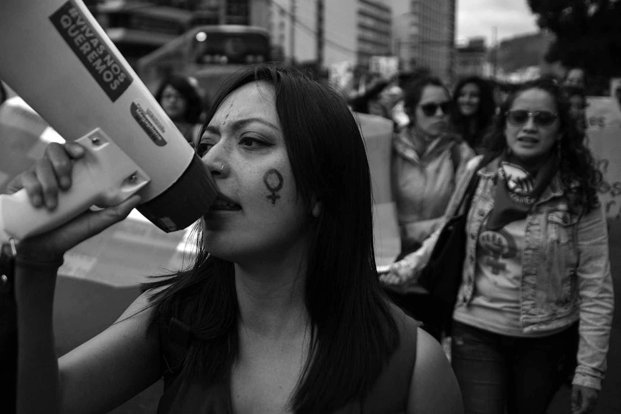 Une femme munie d'un haut-parleur manifeste dans la rue avec d'autres femmes.