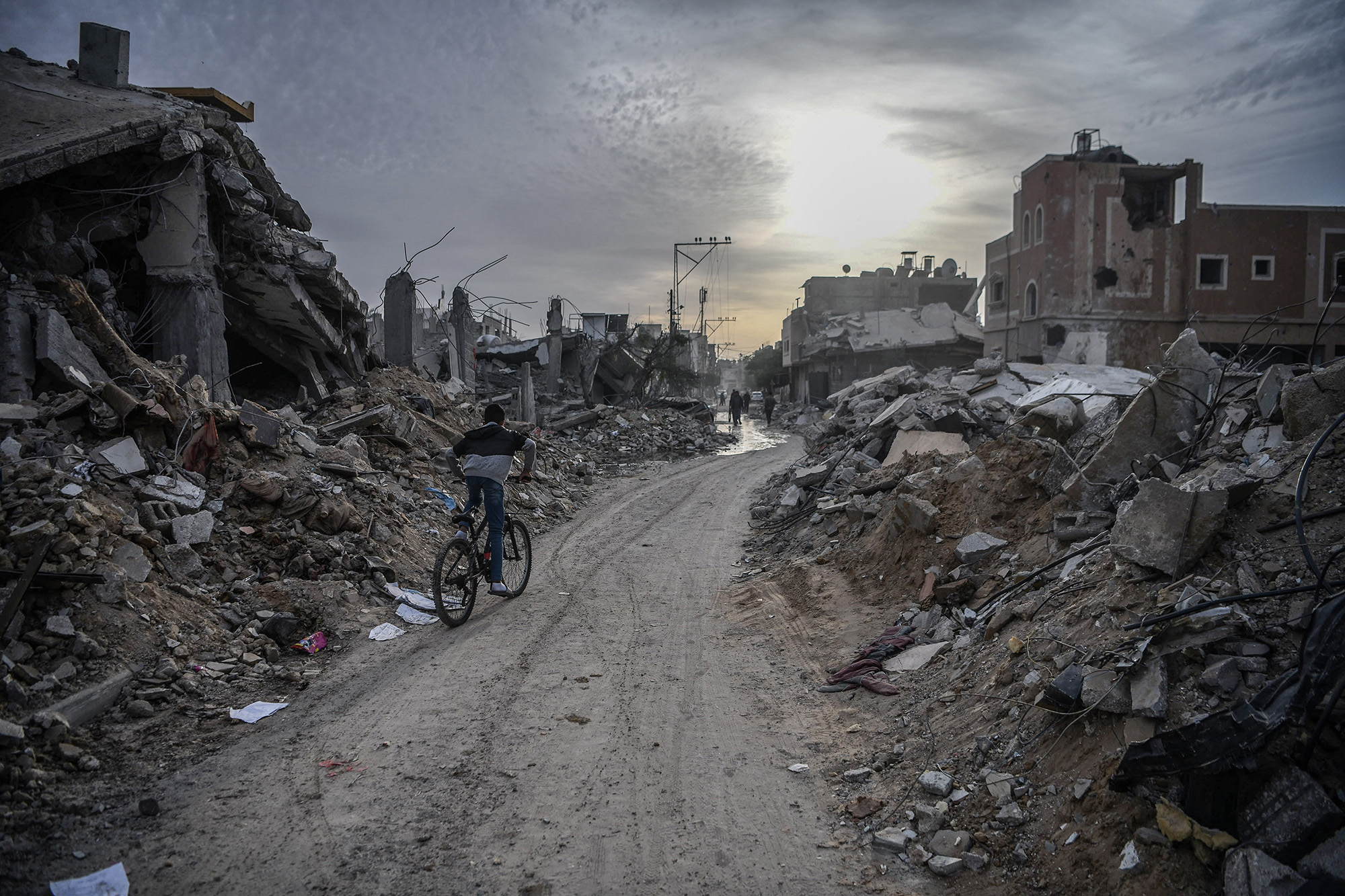 A young boy, riding a bicycle, passes through a group of destroyed houses in Gaza.