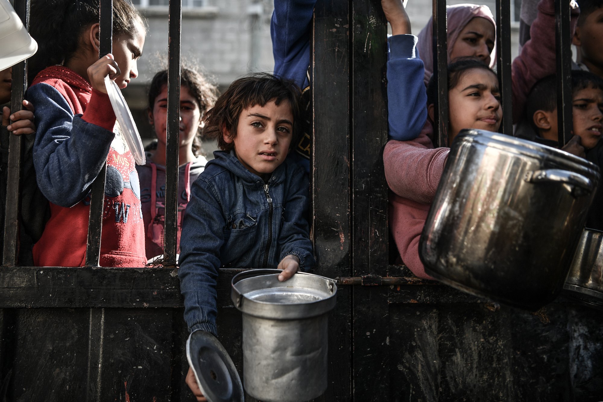children and women holding container from behind bars