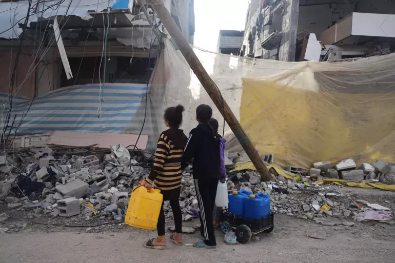 children carrying water containers amid rubble