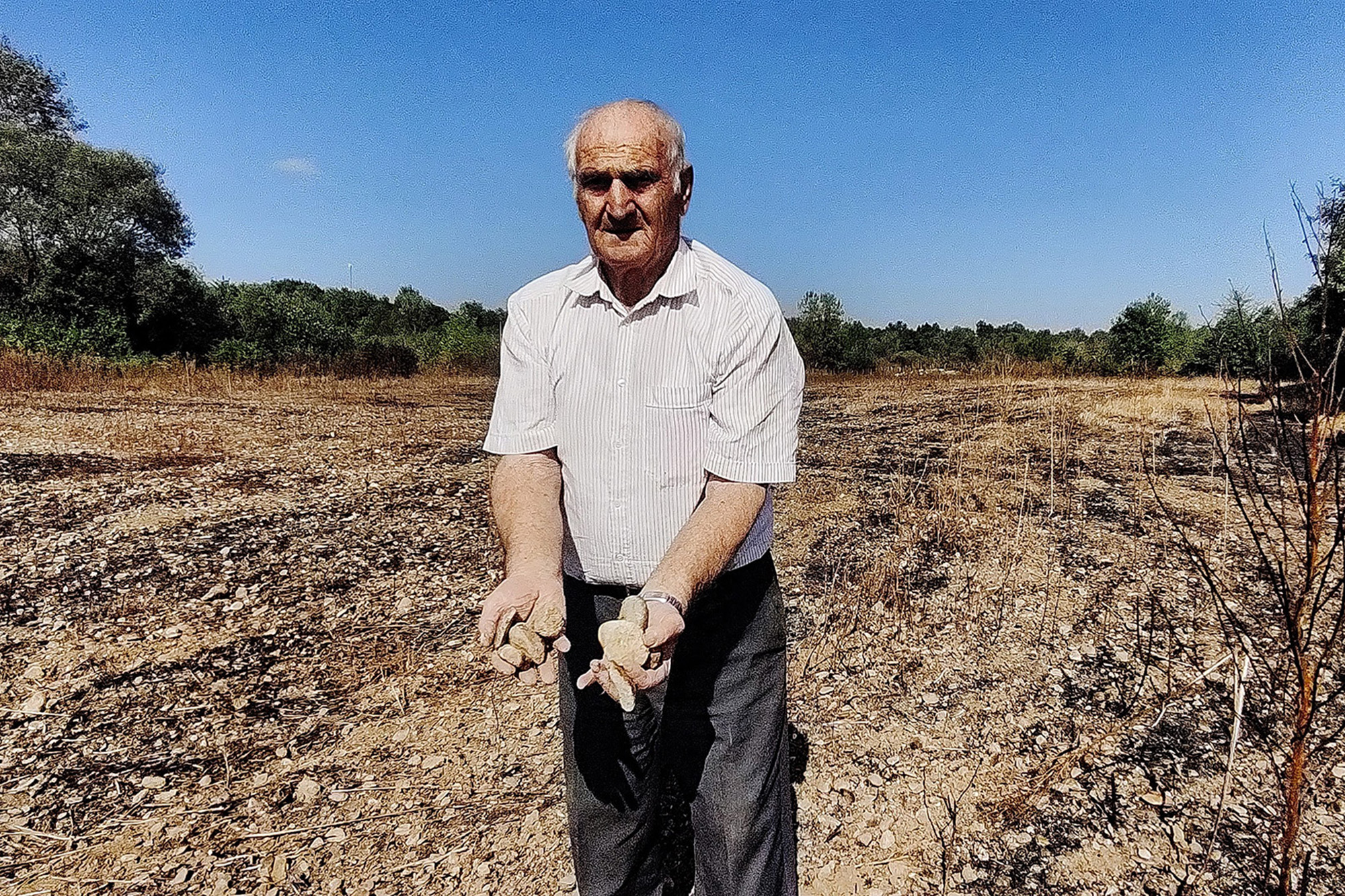 A Kosovan farmer shows the stones left after the floods that destroyed his wheat field. 