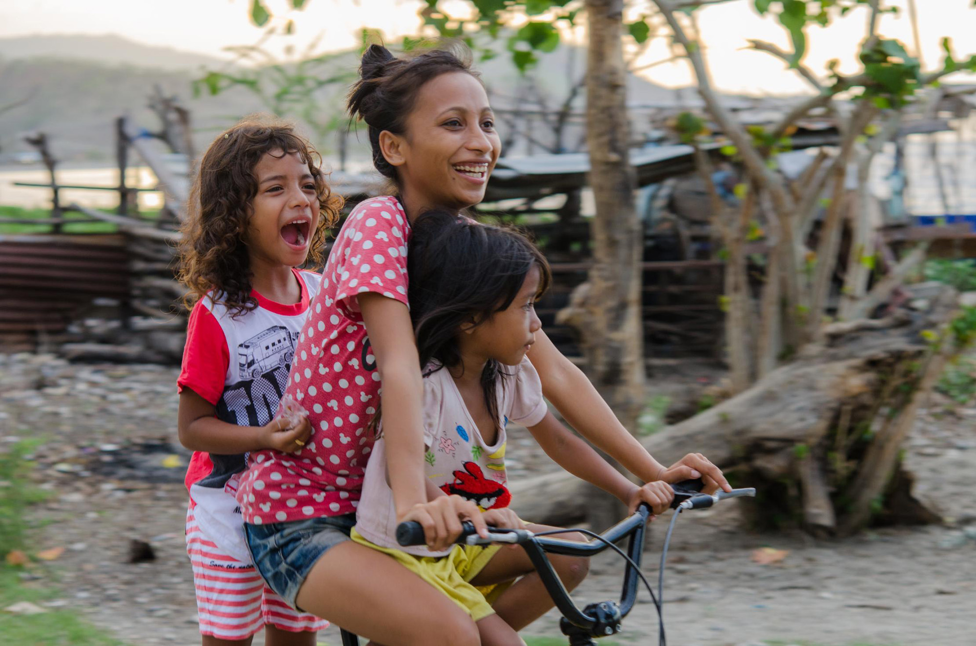 Three girls riding on the same bicycle in Timor Leste.
