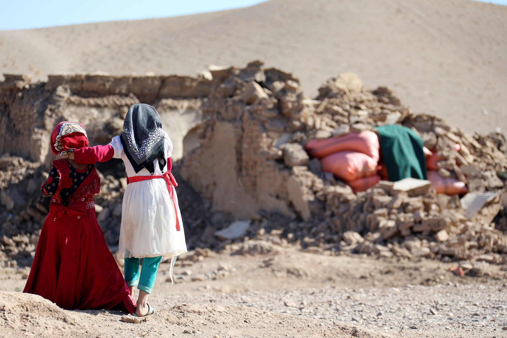 Two young children walking through an earthquake site. 