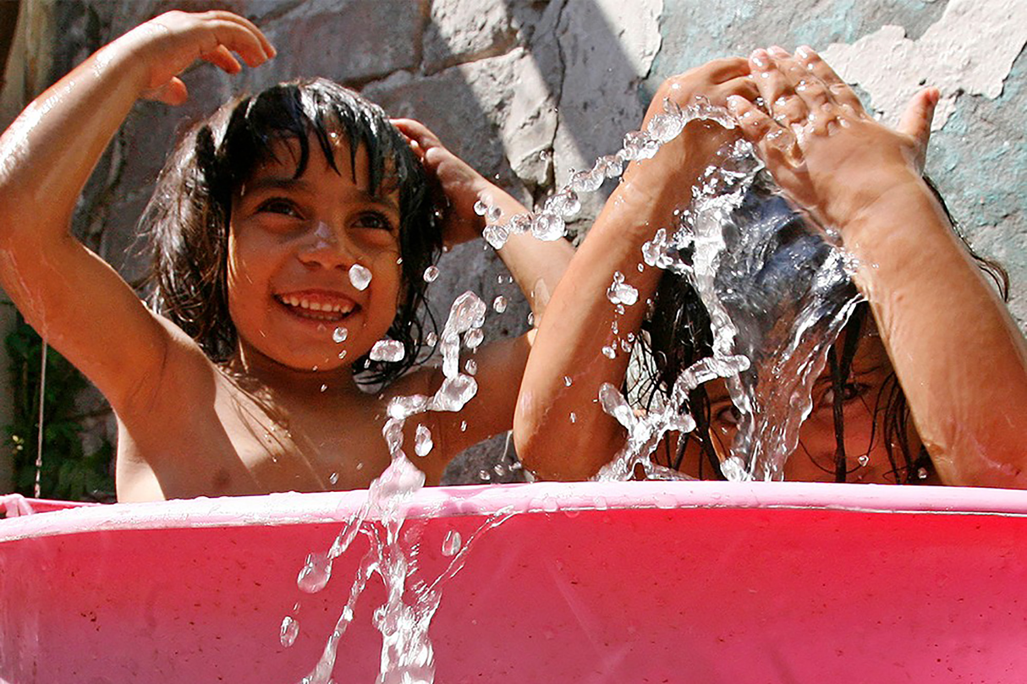 Deux enfants roms jouant avec de l'eau dans un petit bassin.