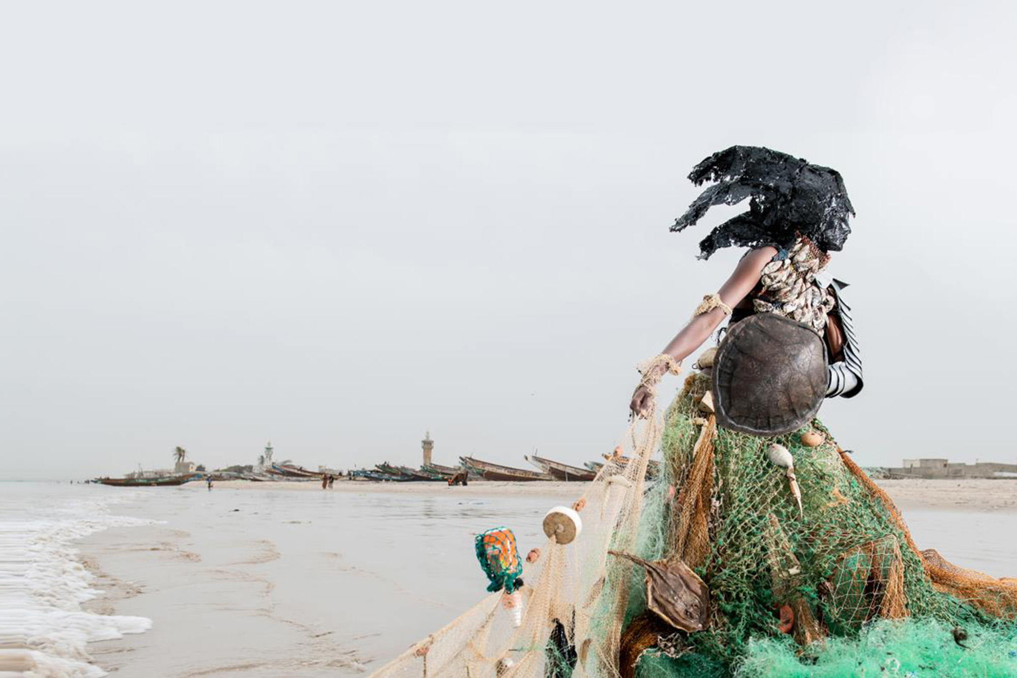 Représentation artistique d'une femme en train de lutter contre la pollution de l'eau sur une plage. Elle porte une robe faite d'un filet de pêche.