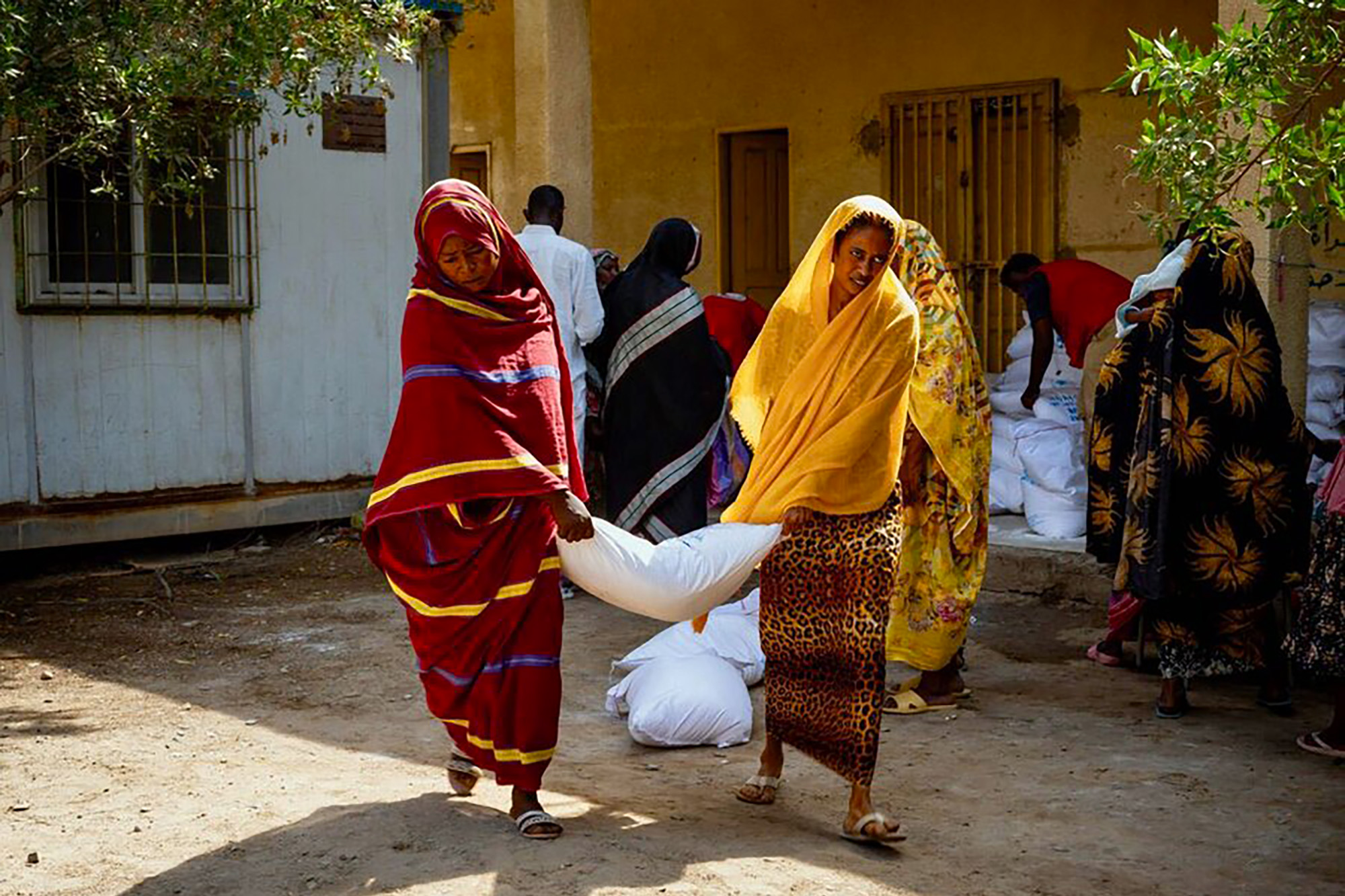 Two women carrying a sack of food assistance.