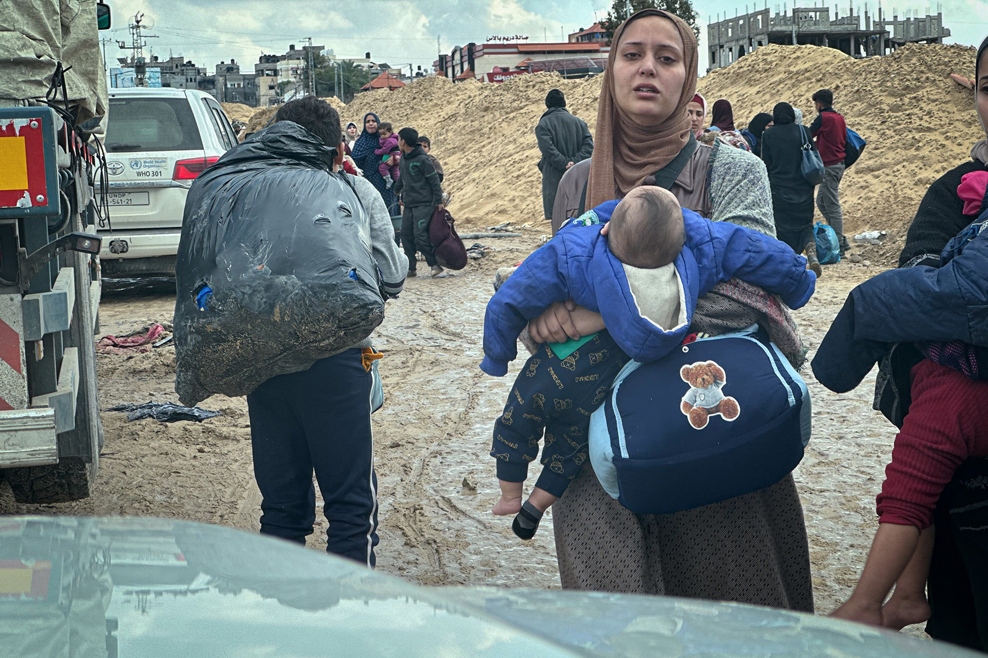 A woman carries a baby on a Gaza Street. People flee the bombing with the few belongings they can carry.