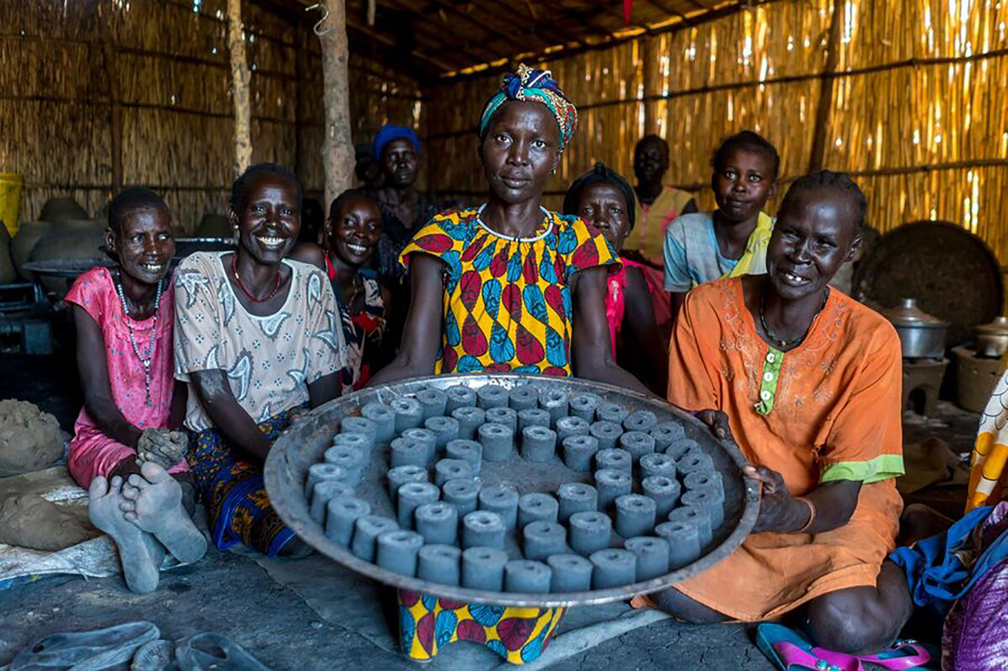 A woman showing a plate of charcoal briquettes made from charred water hyacinths, an invasive species that disrupts waterways and aquatic food systems.