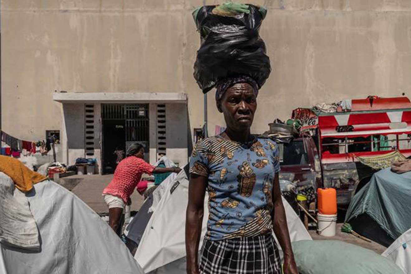 Une femme haïtienne portant sur sa tête un sac rempli d'affaires 