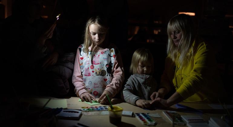 Deux enfants dessinent dans un environnement sombre, éclairés par une lampe frontale portée par un adulte à leurs côtés