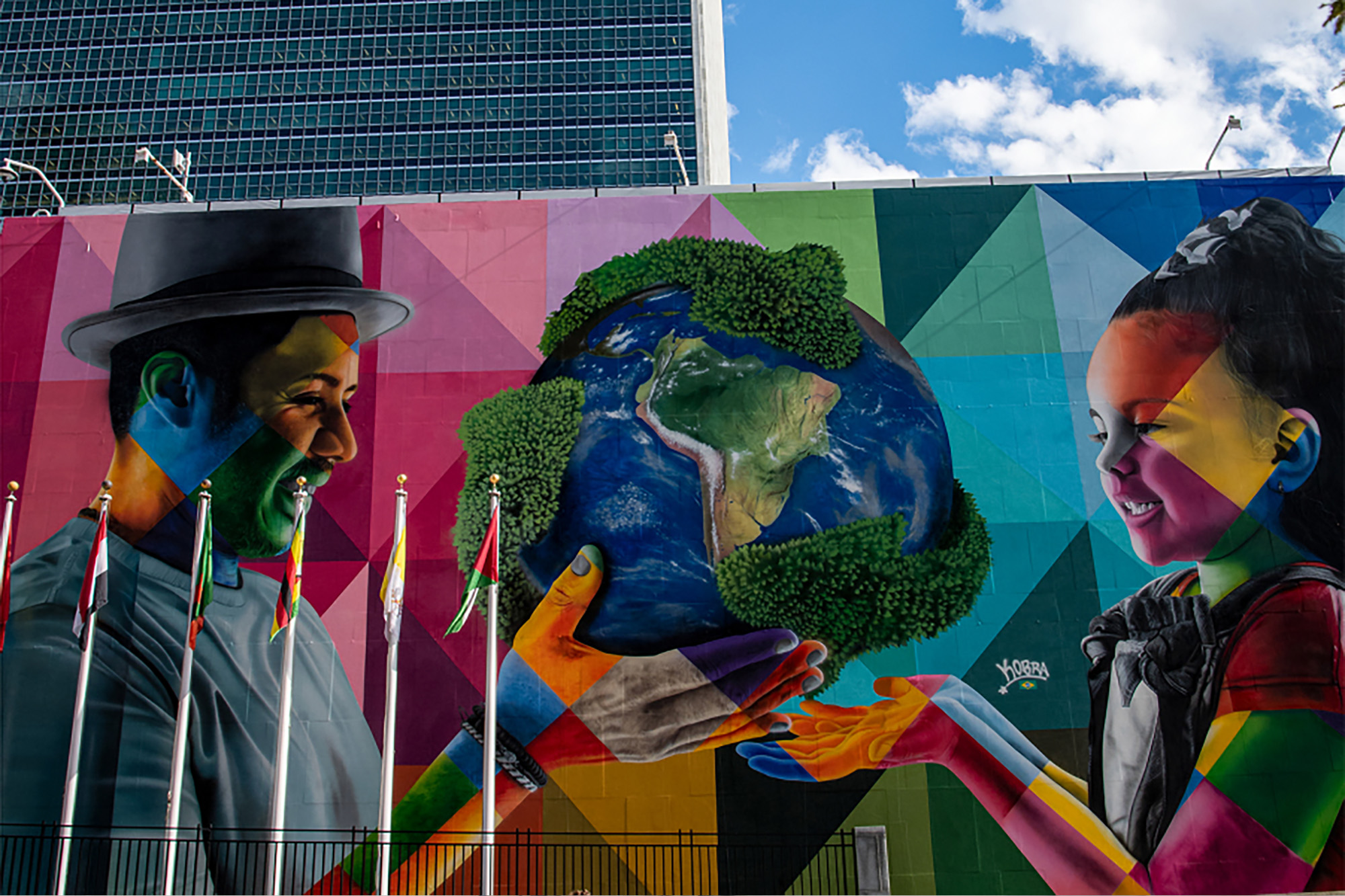 View of the Eduardo Kobra mural at UN Headquarters depicting a man handing an Earth globe to a young girl.