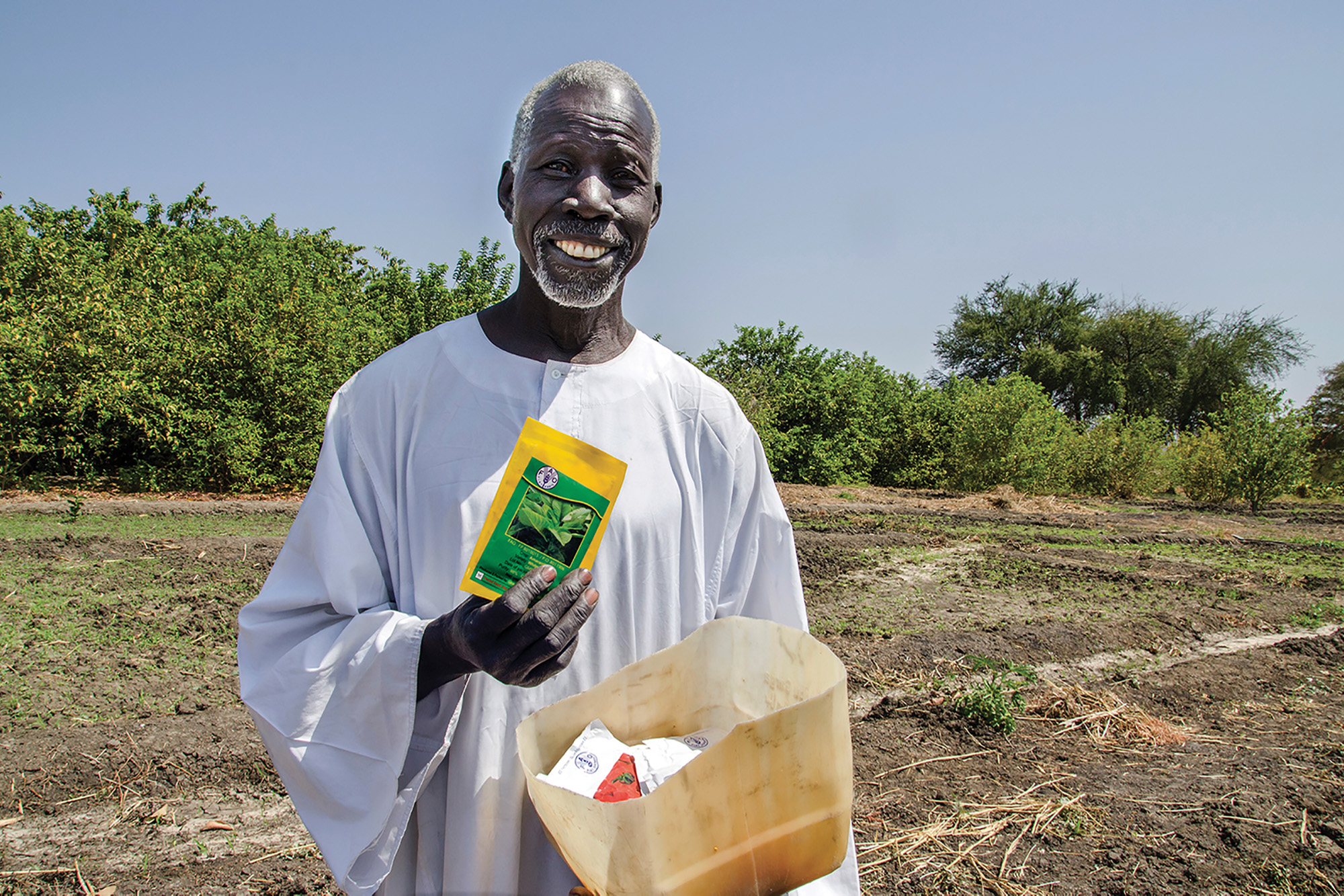 An elderly farmer in South Sudan, rebuilding homes after an emergency, holding seeds.