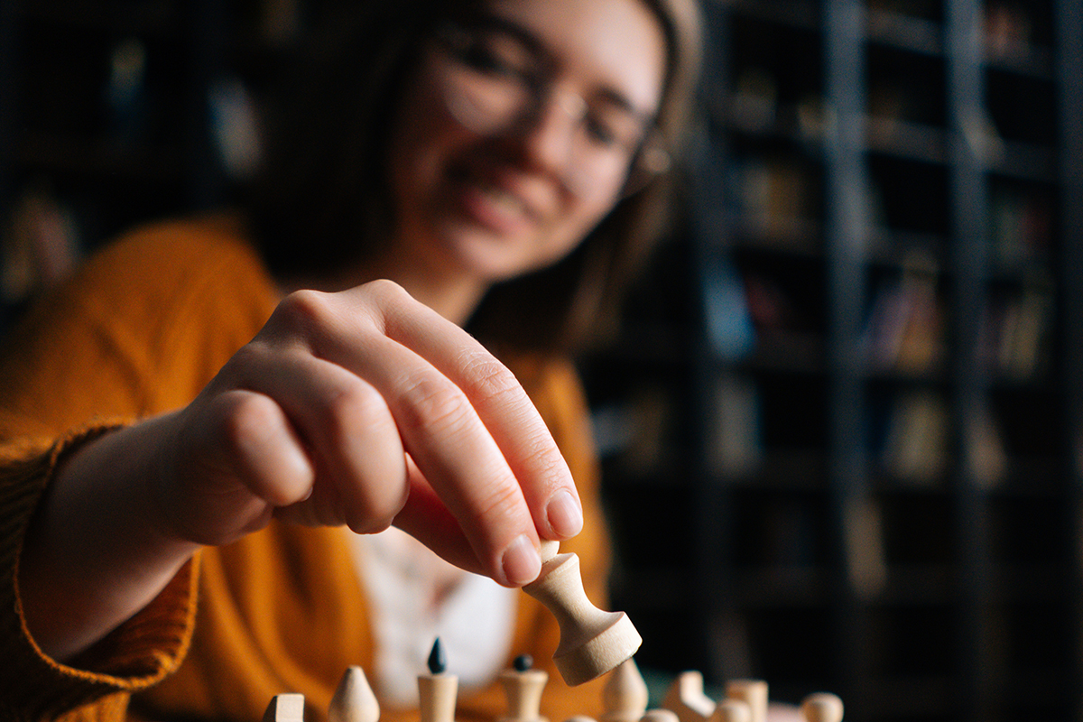 smiling woman makes a chess move in dark library room