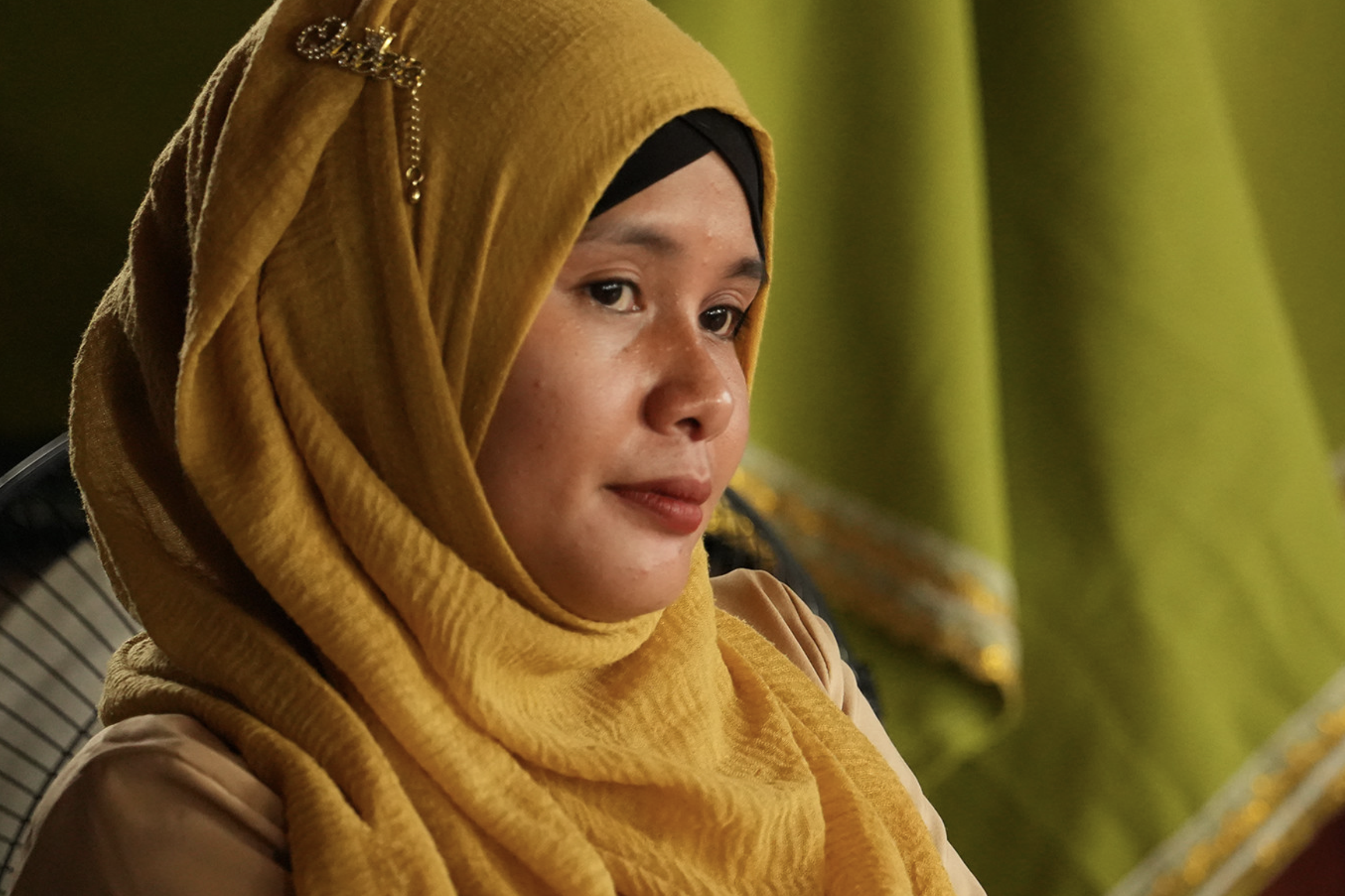 A photograph showing a woman in yellow clothing in profile against a green background