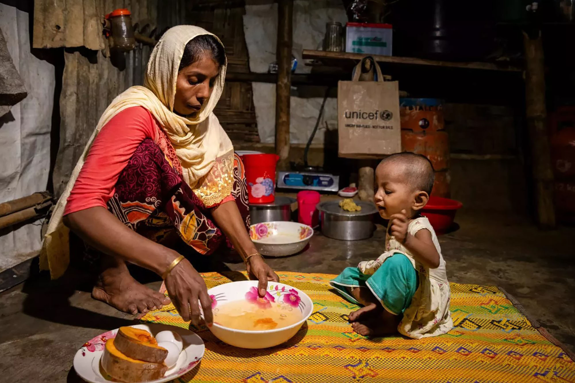 A Rohingya woman shares a bowl of food with her child.