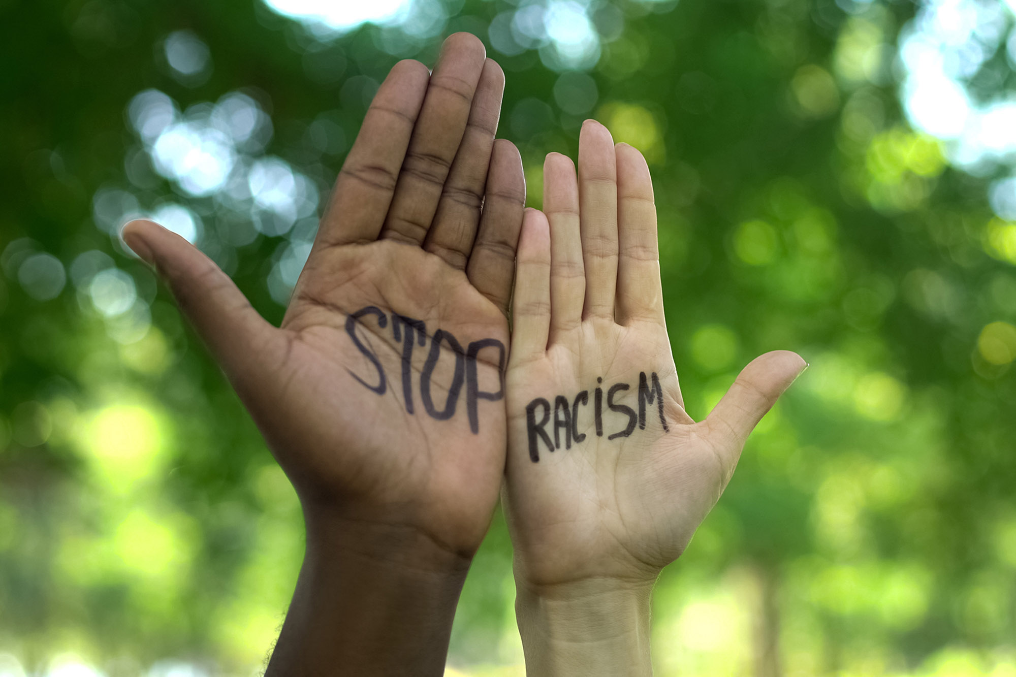 Two people of different skin colors show a Stop Racism message painted on their hands.