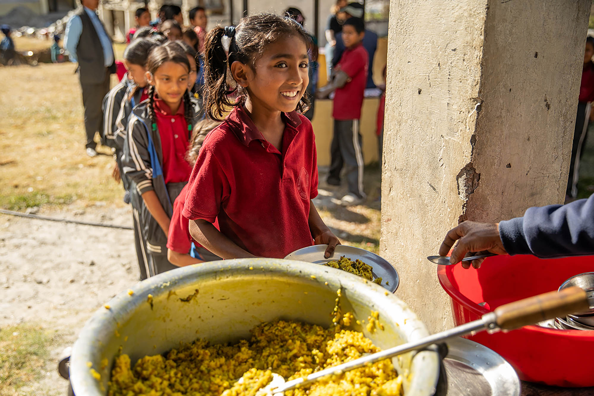 A girl smiles while she gets a plate of food at her school.
