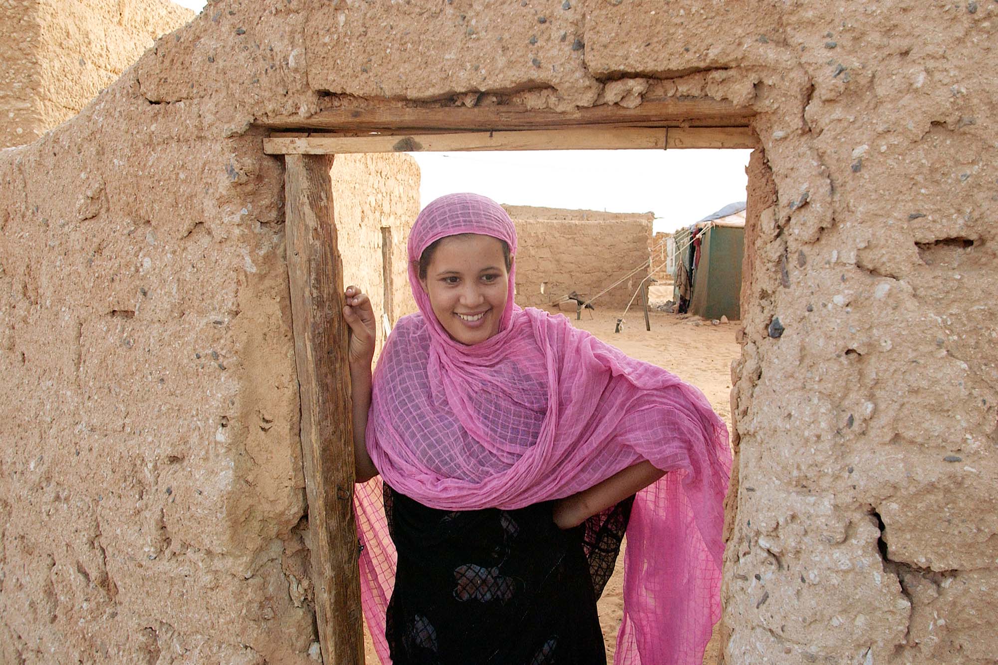 A smiling African woman stands in a doorway of a refugee camp.