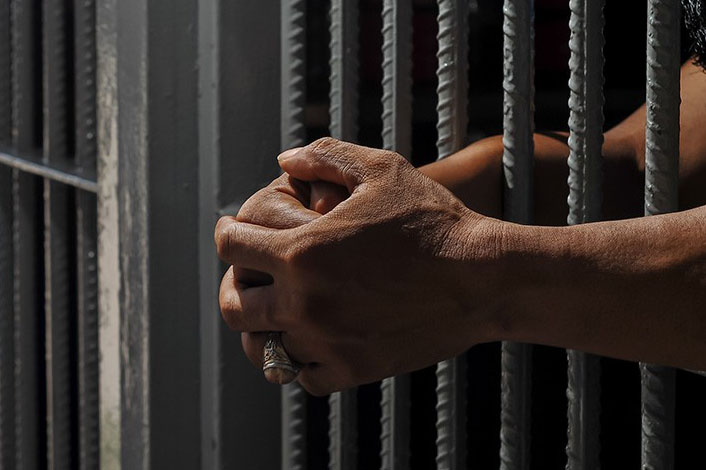 A pair of hands behind bars.