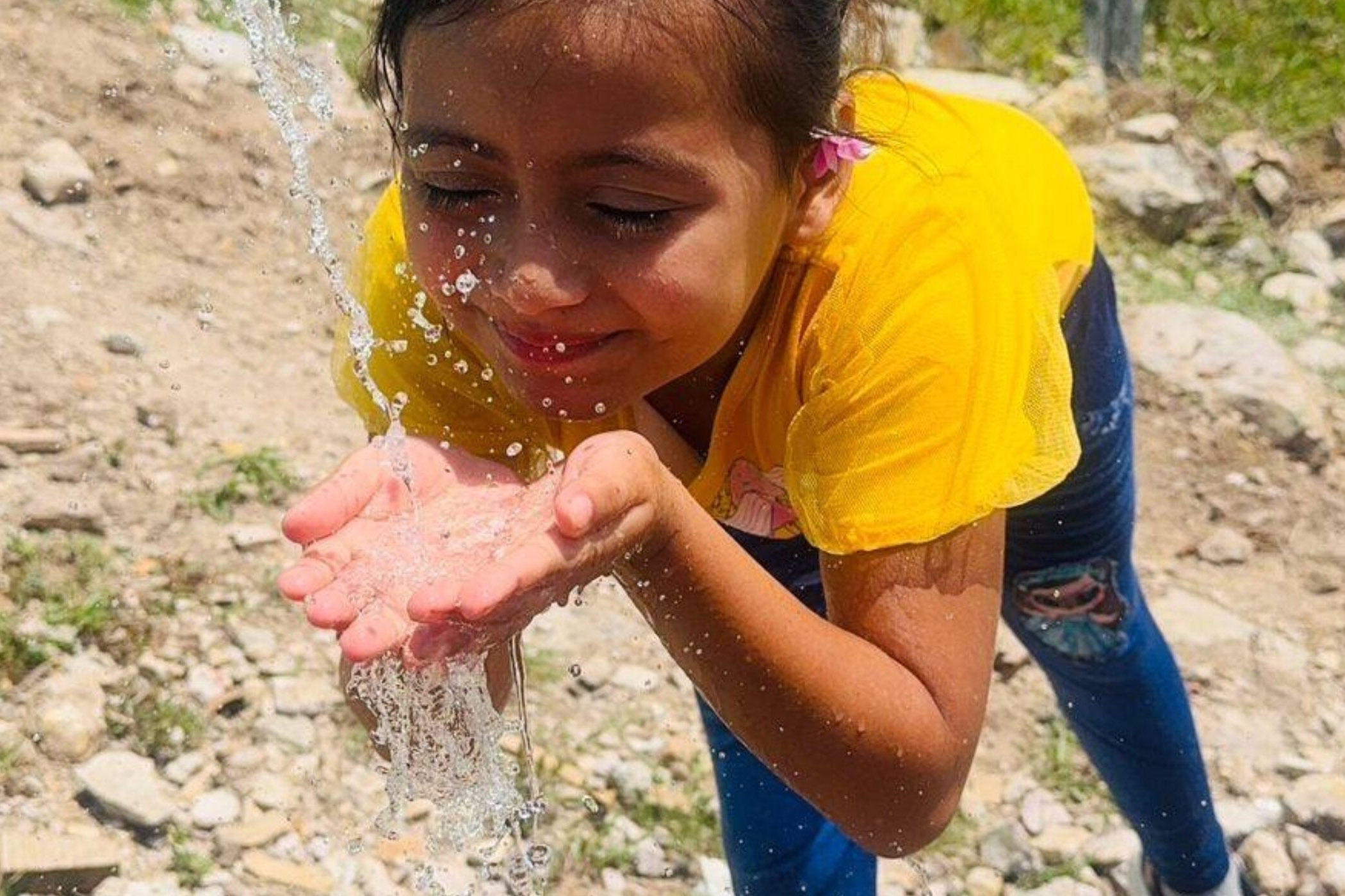 A young girl taking in a drink of piped water