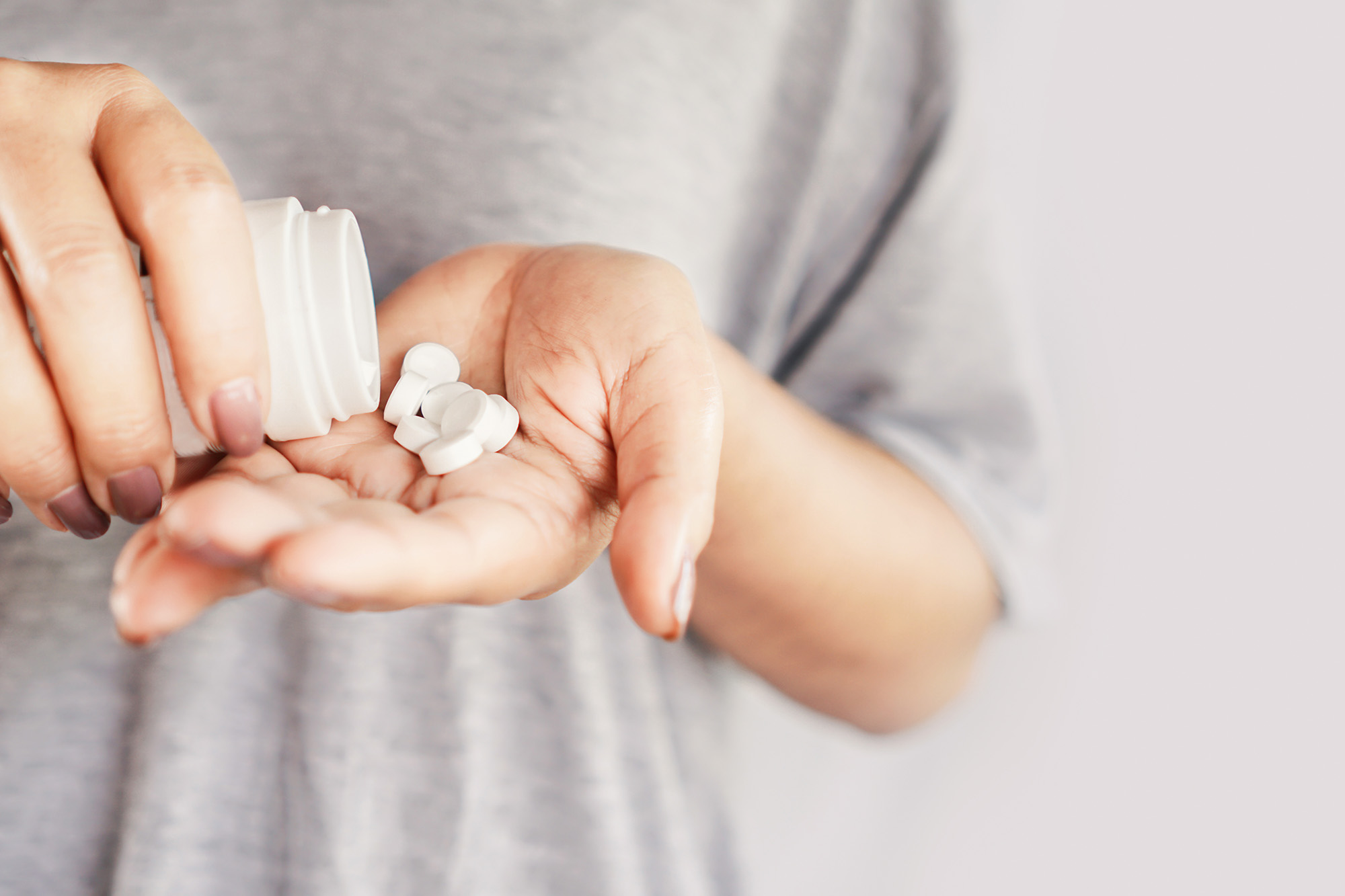 Close-up of a woman's hand holding a medicine bottle and taking an overdose of pills.