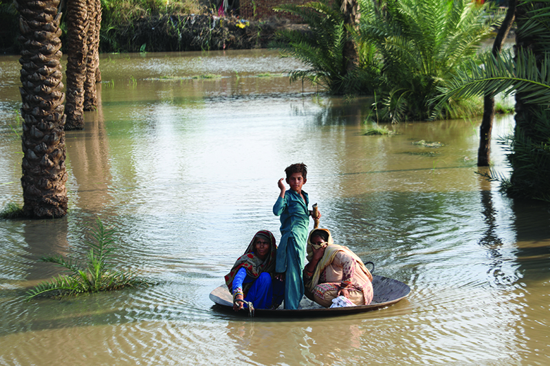 Two women and a child stand in a makeshift raft in the middle of a flooded area.