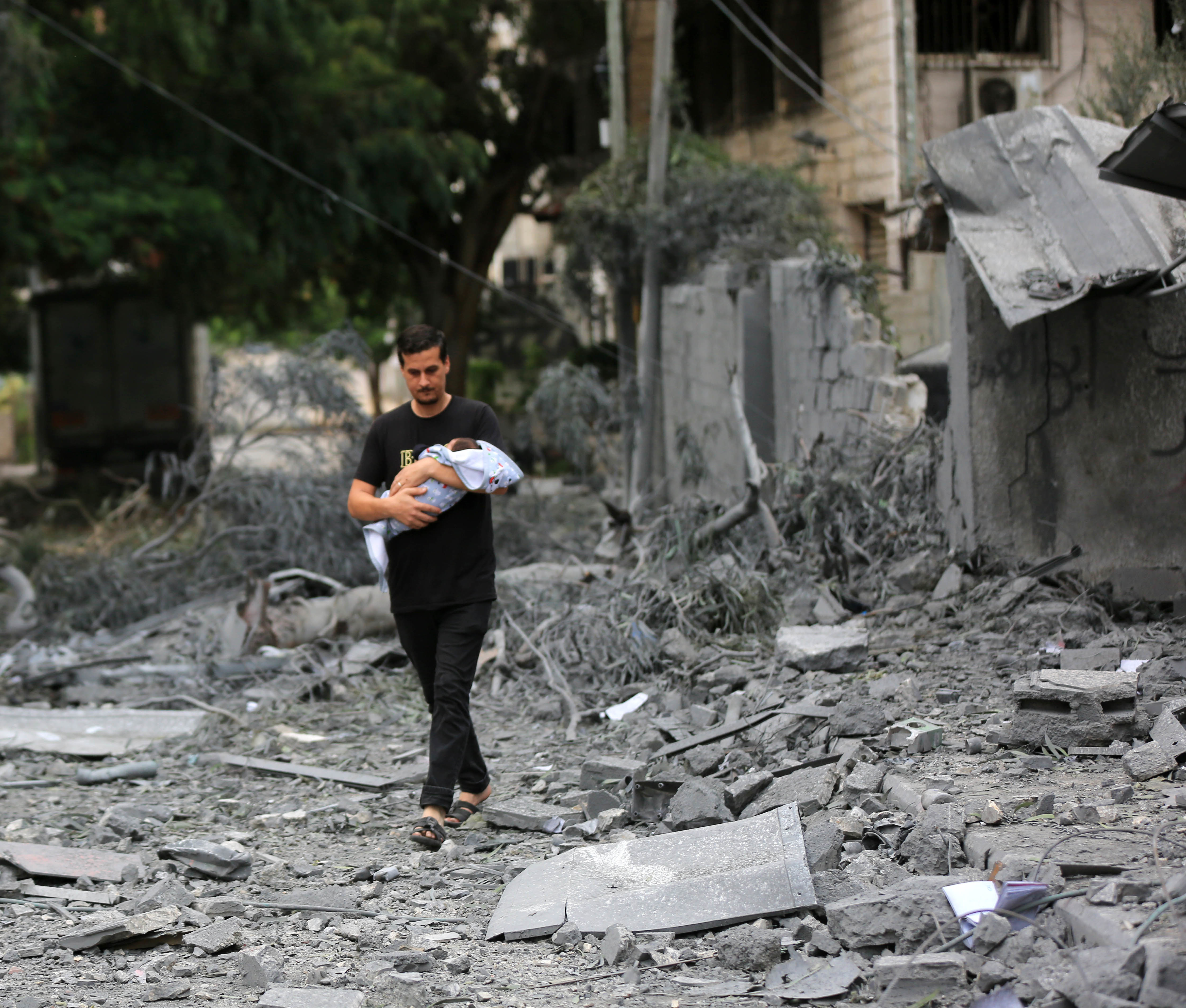 un hombre caminando entre los escombros de los edificios derrumbados, con un bebé en brazos
