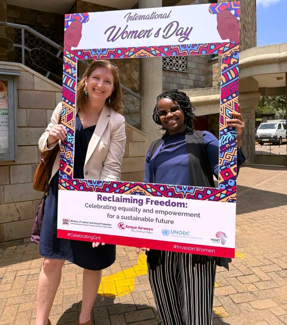 Carmen poses with Winnie as they hold a window prop with the text 'international women's day' written on it