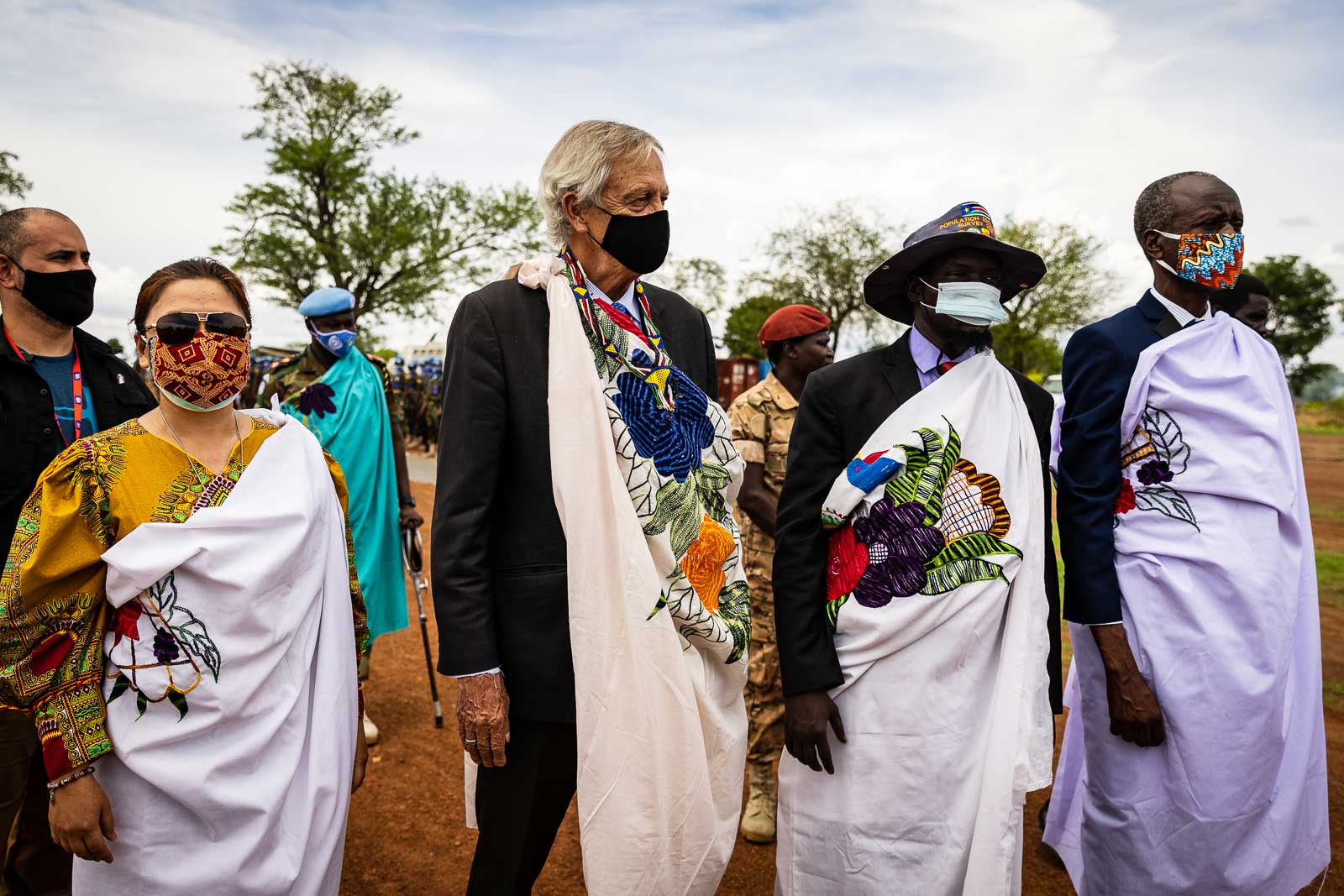 Nicholas standing amongst people. They are all wearing face masks and have decorated fabrics draped across their shoulders.