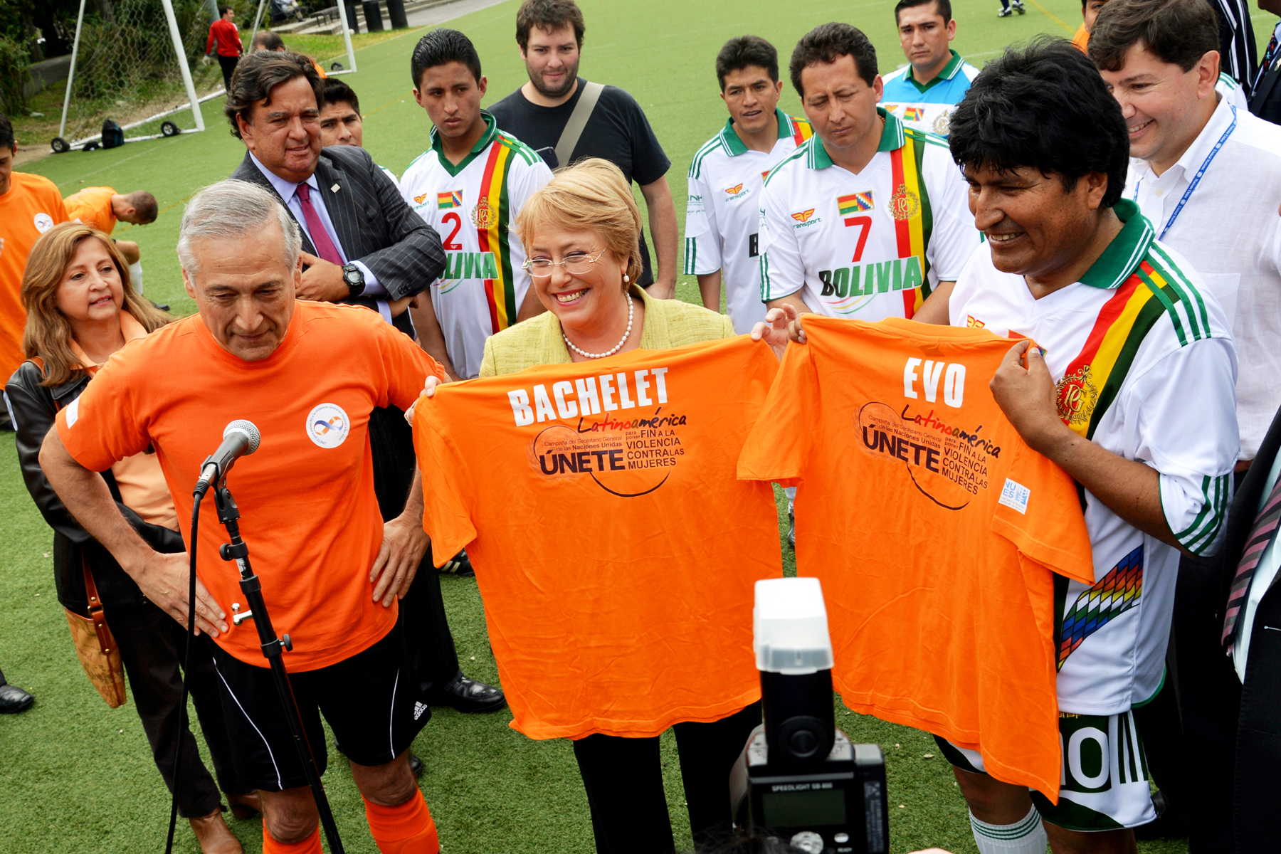 Michelle Bachelet, along with other dignitaries, are standing in a soccer field, proudly holding up orange t-shirts advocating to end all forms of violence against women and girls.