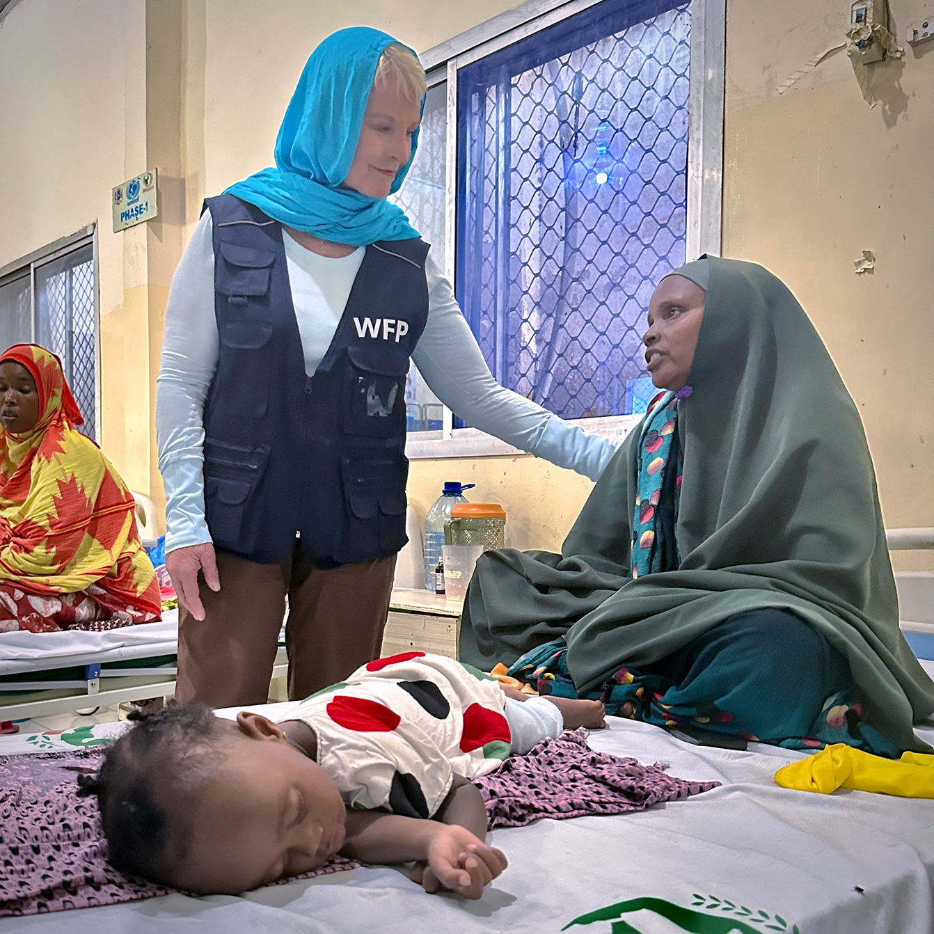 Cindy in a clinic with her hand on a mother's shoulder. A child lying on the hospital bed next to them.