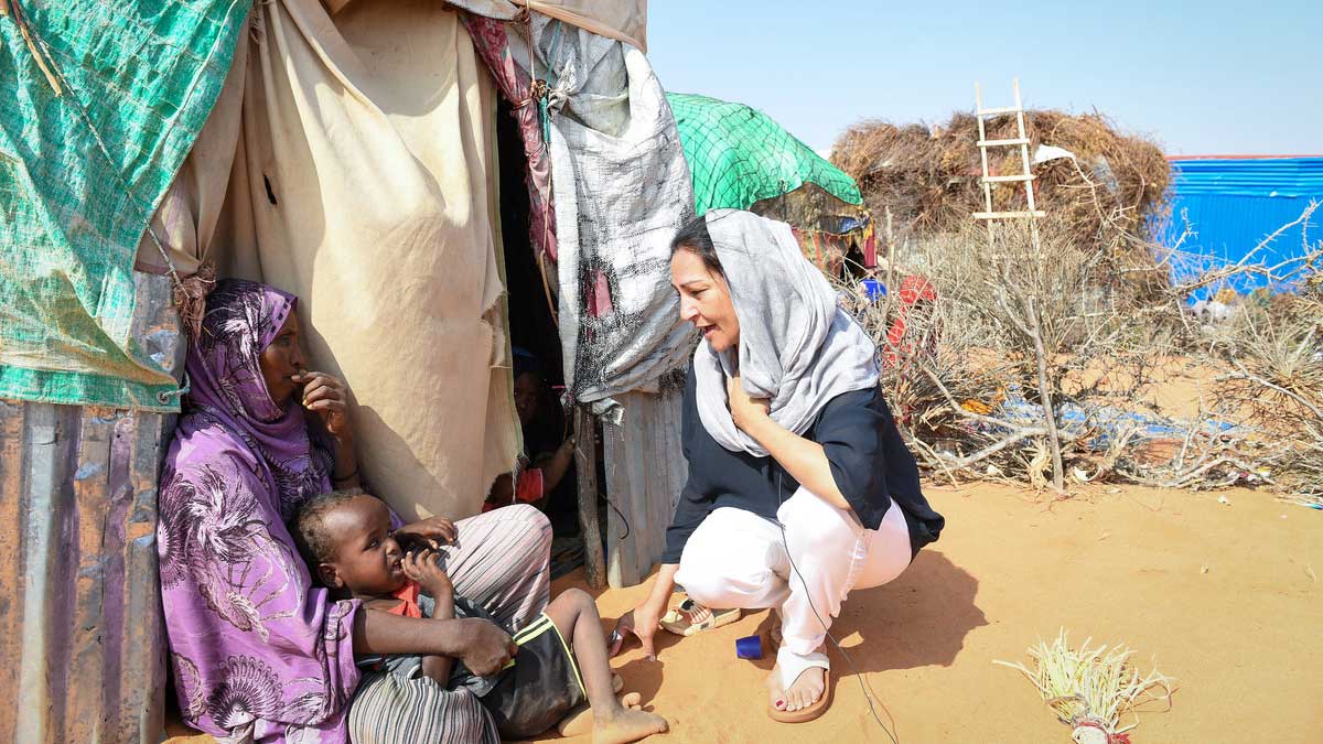 Reena interacts with a mother and child who are sitting next to a tent