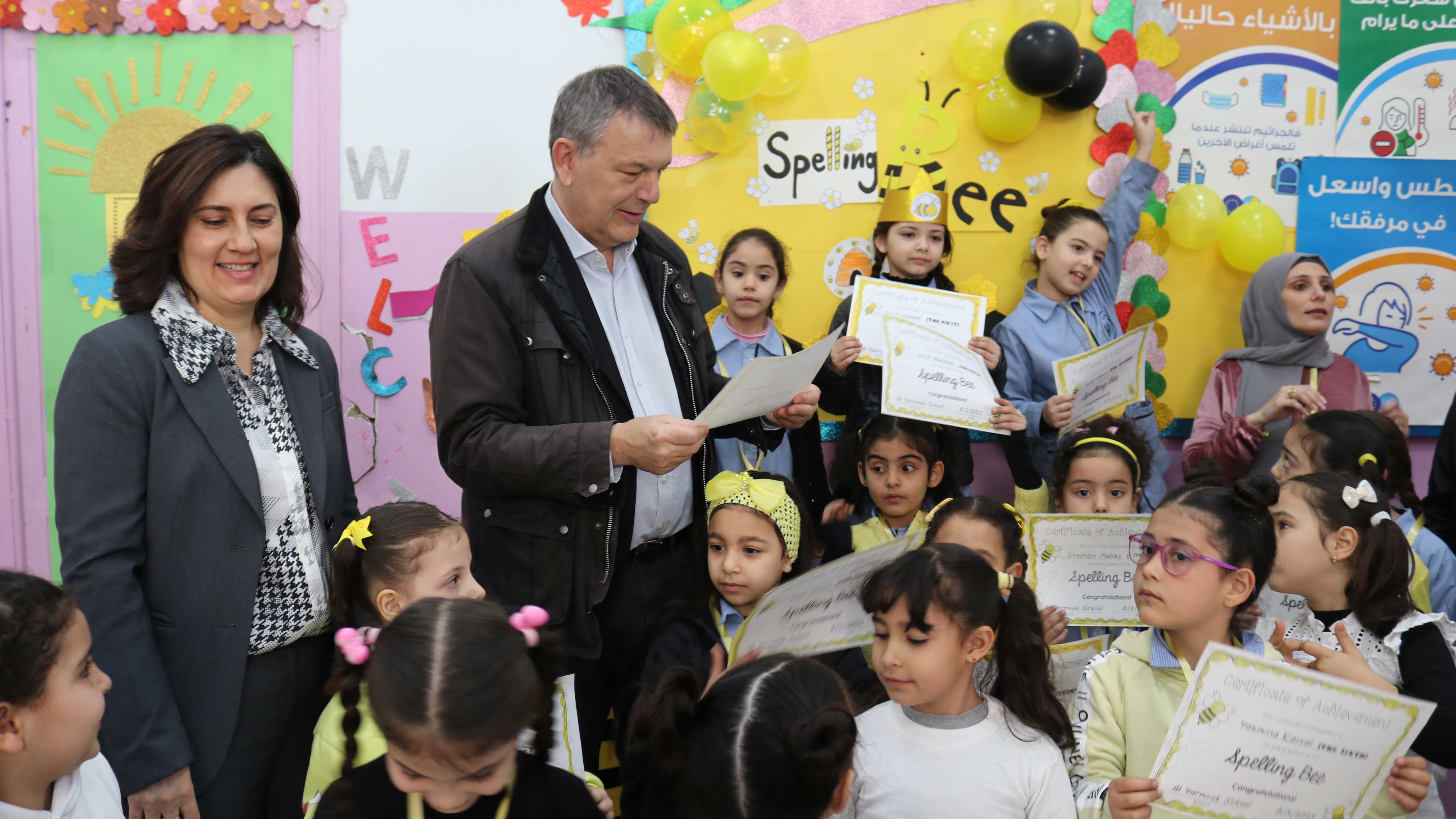 Lazzarini stands amongst childten in a school with a woman next to him.