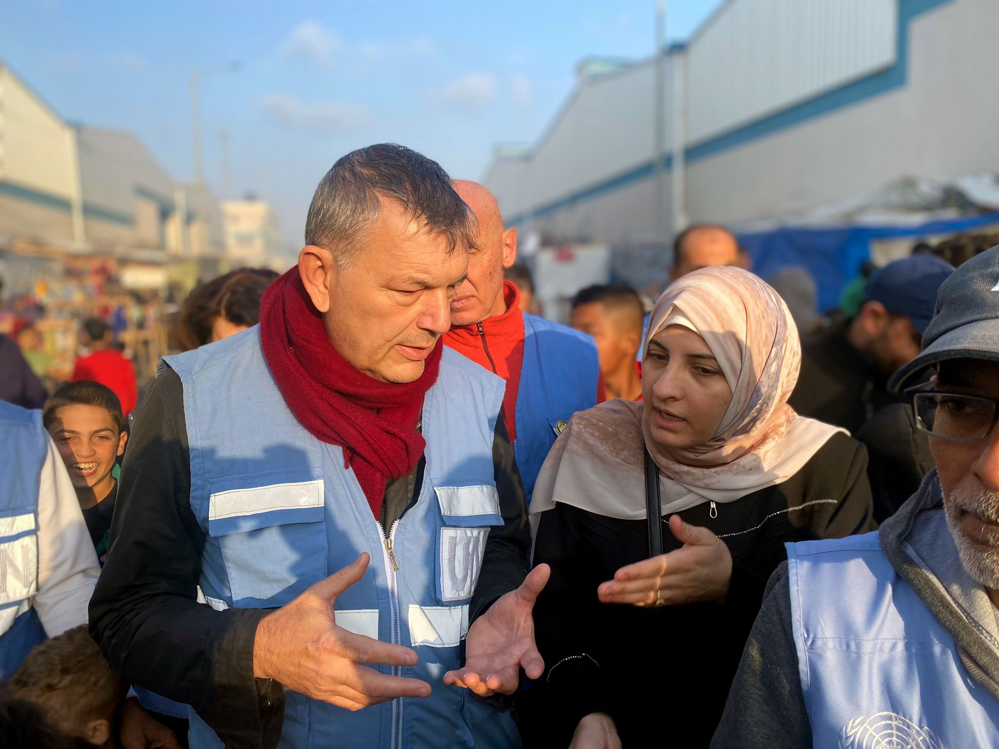 In a throng of people, Lazzarini - wearing an UNRWA blue vest - walks outdoors and chats with a woman - herself wearing a veil.