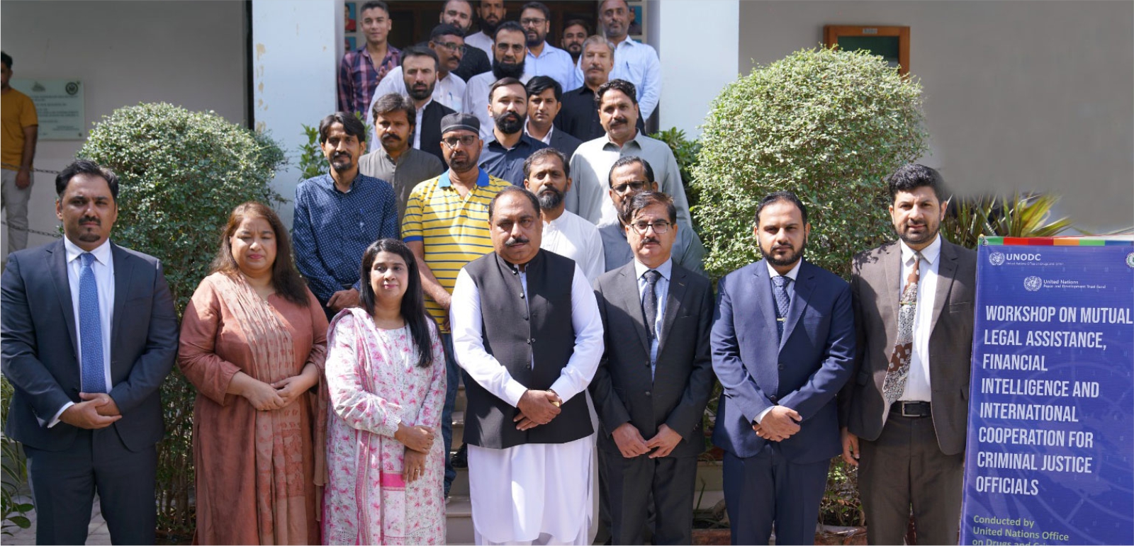 group photo of the men and women on the steps leading into a building with a poster announcing the workshop to their left